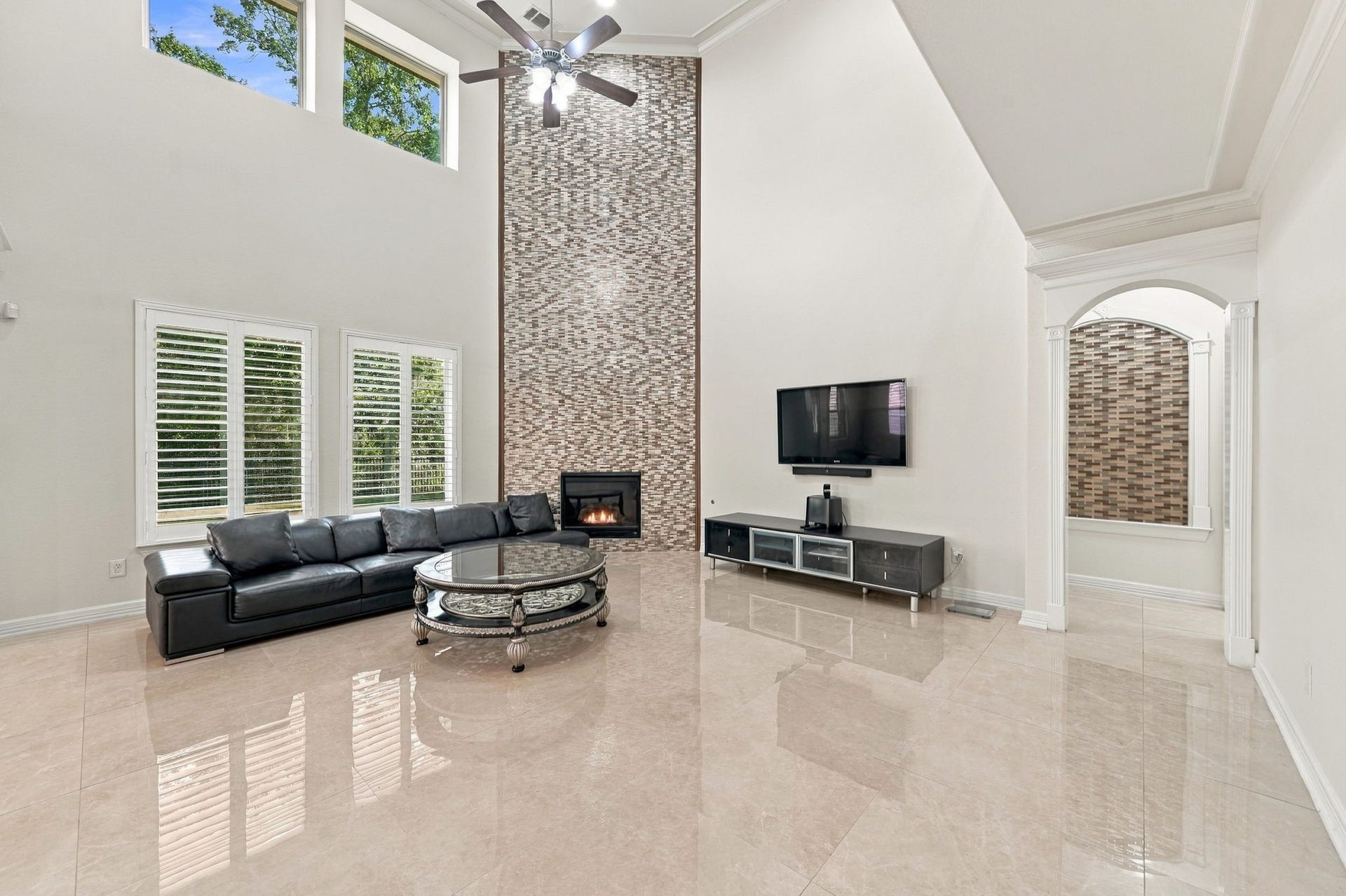 5411 Oban Terrace Lane, Sugar Land, TX 77479 A beautiful fireplace framed by a striking floor-to-ceiling mosaic tile accent wall and impressive two-story windows makes this living room a standout space for cozy evenings, family gatherings, and everyday enjoyment.
