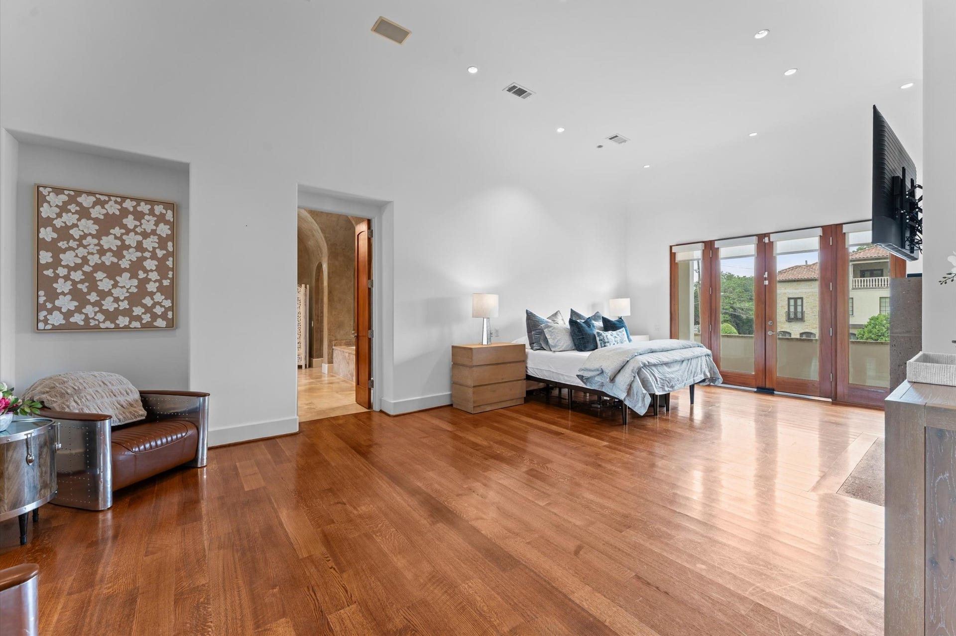 5135 Longmont Drive, Houston, TX 77056 A spacious primary bedroom showcases rich mahogany flooring, a striking stone fireplace, and multiple private balconies overlooking the estate grounds.