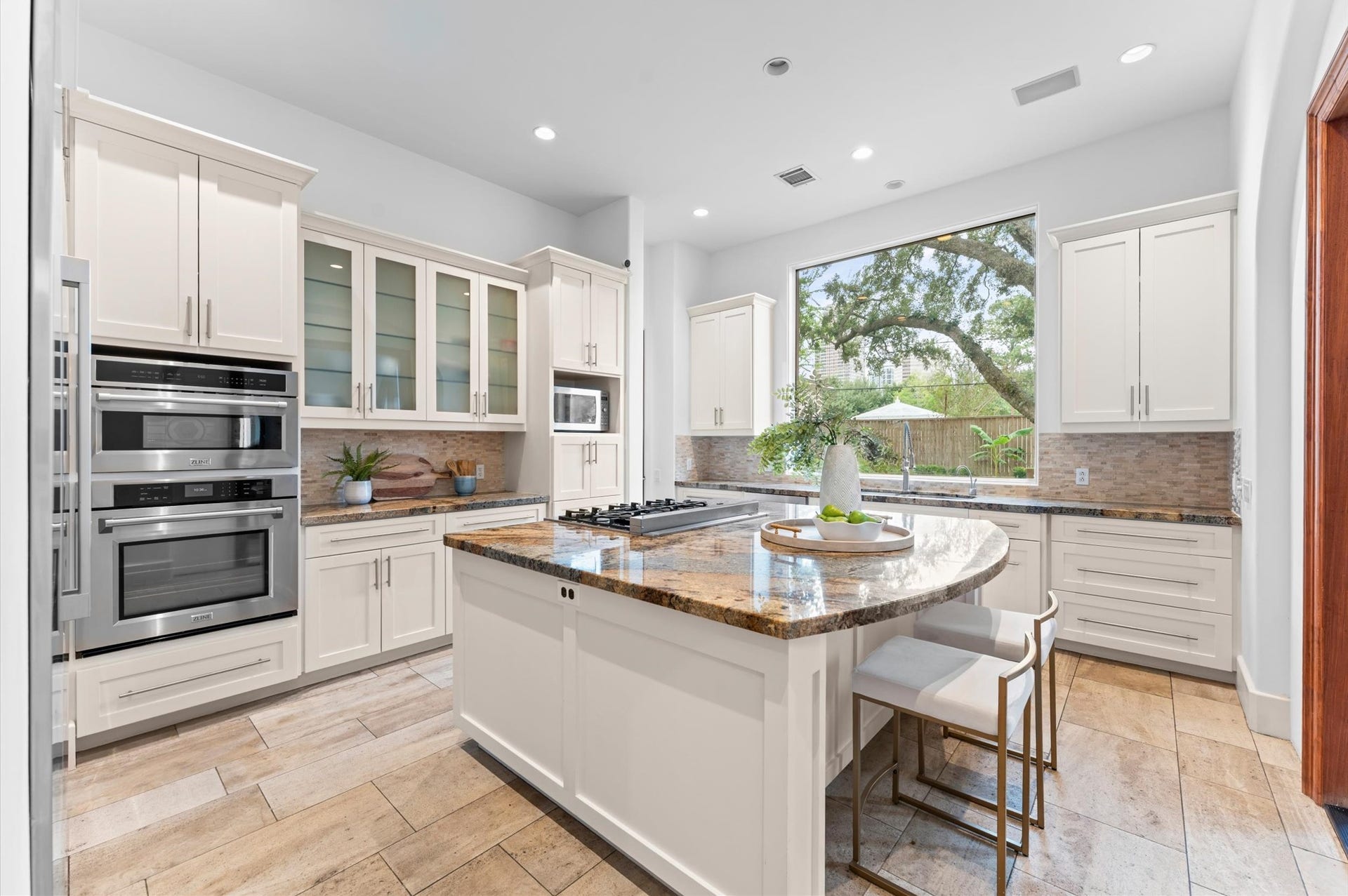 5135 Longmont Drive, Houston, TX 77056 The spacious gourmet kitchen features freshly painted cabinetry, granite countertops, a designer backsplash, travertine flooring, and an expansive island with a gas cooktop. A premium stainless steel appliance suite, including a full-size refrigerator and freezer, complements the kitchen's functional design, while a walk-in pantry provides additional storage.