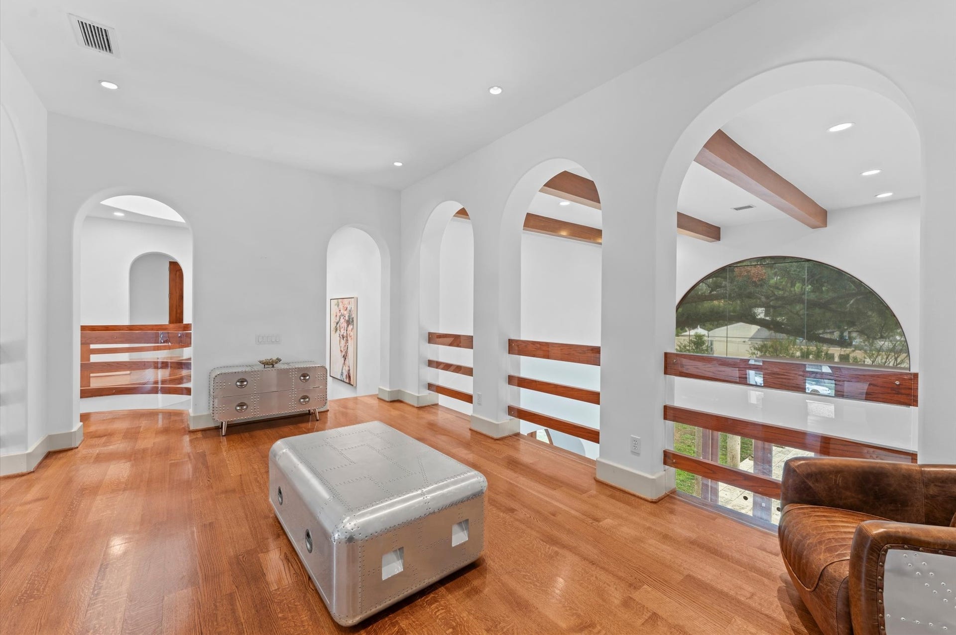 5135 Longmont Drive, Houston, TX 77056 An elegant upper-level gallery featuring warm wood flooring, distinctive arched architectural openings, and custom wood-and-glass railings overlooking the home's dramatic interior.