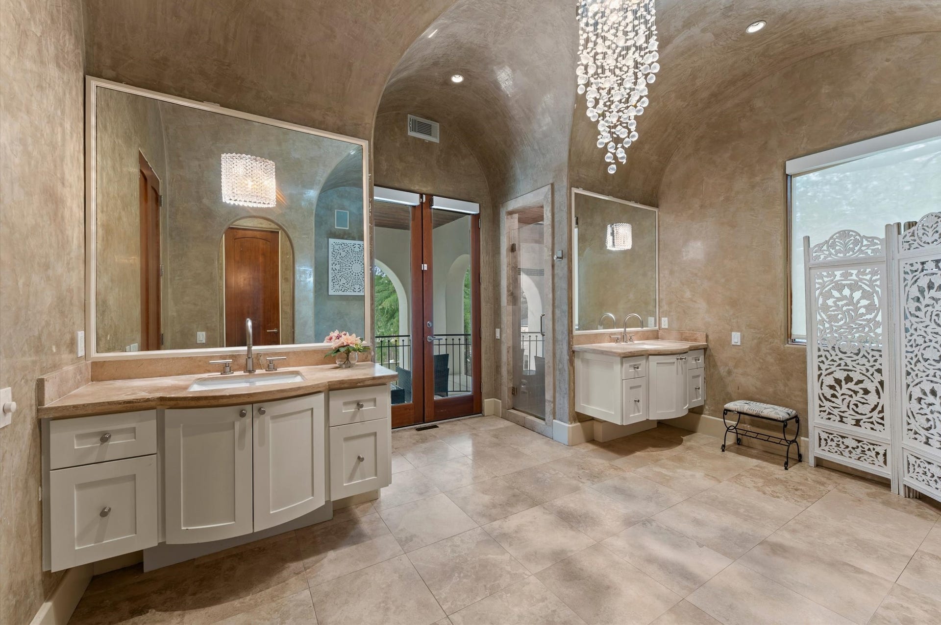 5135 Longmont Drive, Houston, TX 77056 A spa-inspired primary bath features separate floating bombe-style vanities, custom plaster wall finishes, a vaulted ceiling, a glass-enclosed shower, and balcony access.