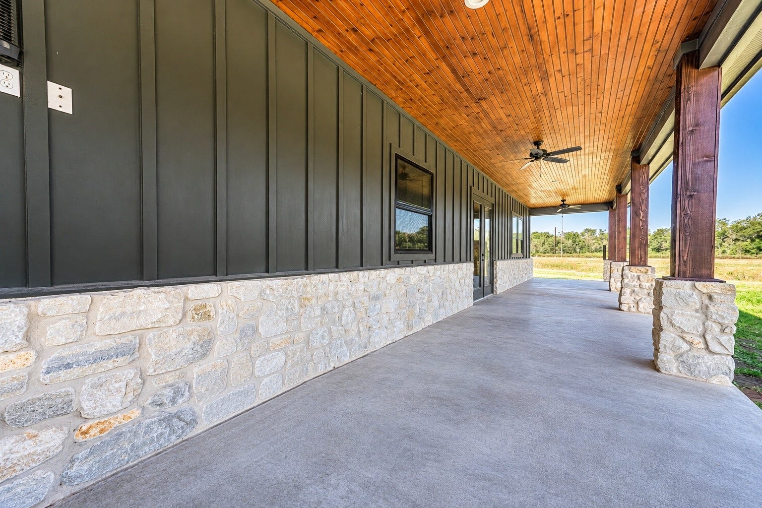 3295 Fm 524 Road, Sweeny, TX 77480 Covered back patio with stained wood ceiling, ceiling fan, stone wainscot and stained concrete floor. This photo may be edited using AI tools.