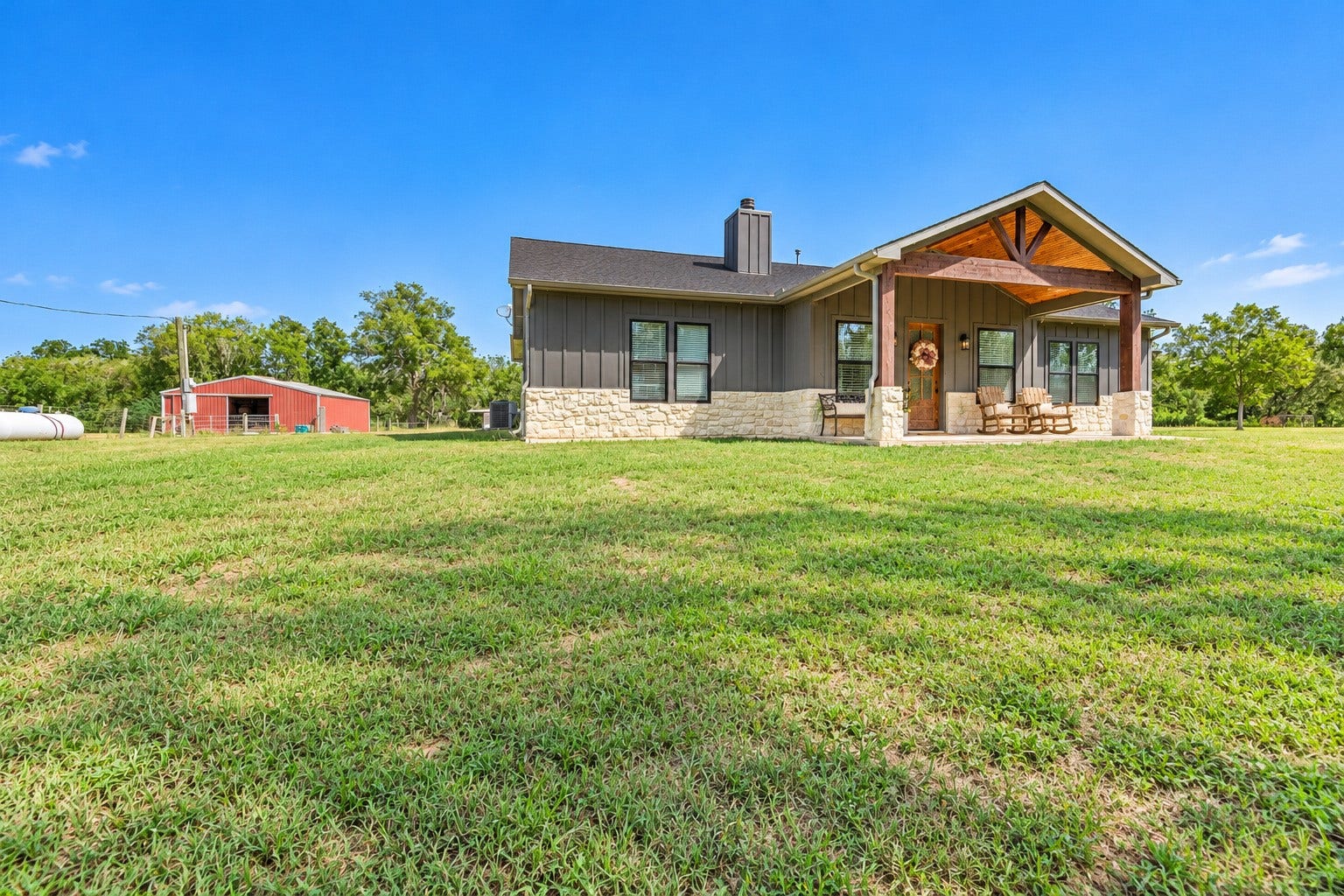 3295 Fm 524 Road, Sweeny, TX 77480 Side exterior of the home with board-and-batten siding and stone accents, with the red barn visible on the left. This photo may be edited using AI tools.