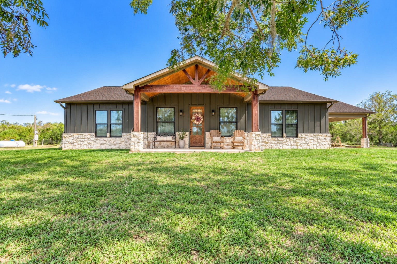 3295 Fm 524 Road, Sweeny, TX 77480 Front exterior of this 2022-built country home on 15.9 acres in Sweeny, TX, with board-and-batten siding, stone wainscot and a covered front porch. This photo may be edited using AI tools.