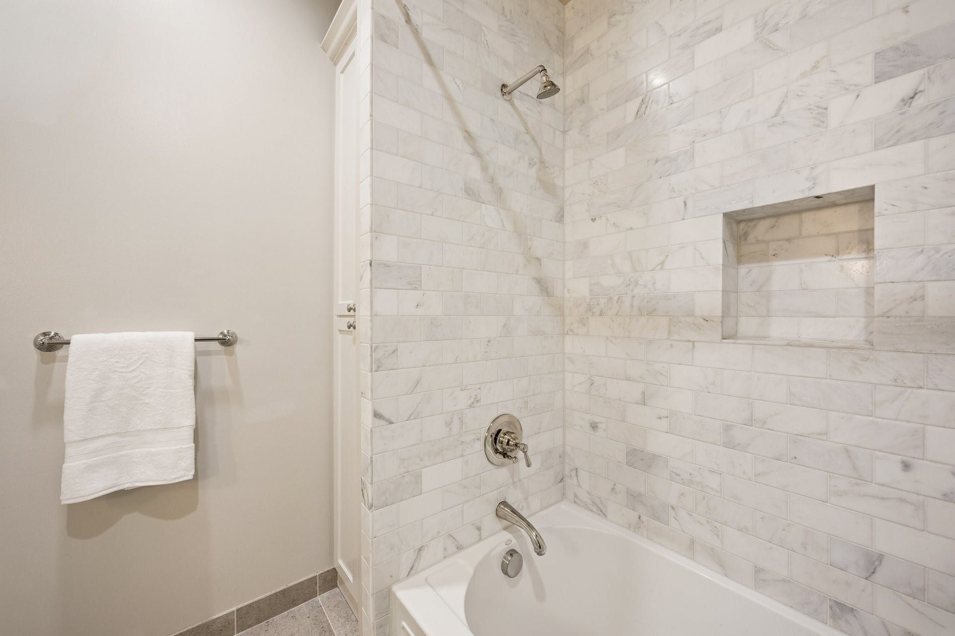 2131 Bancroft Street, Houston, TX 77027 Beautifully tiled tub and shower combination in the first-floor en-suite bathroom, featuring elegant marble-look tile and a built-in shower niche.
