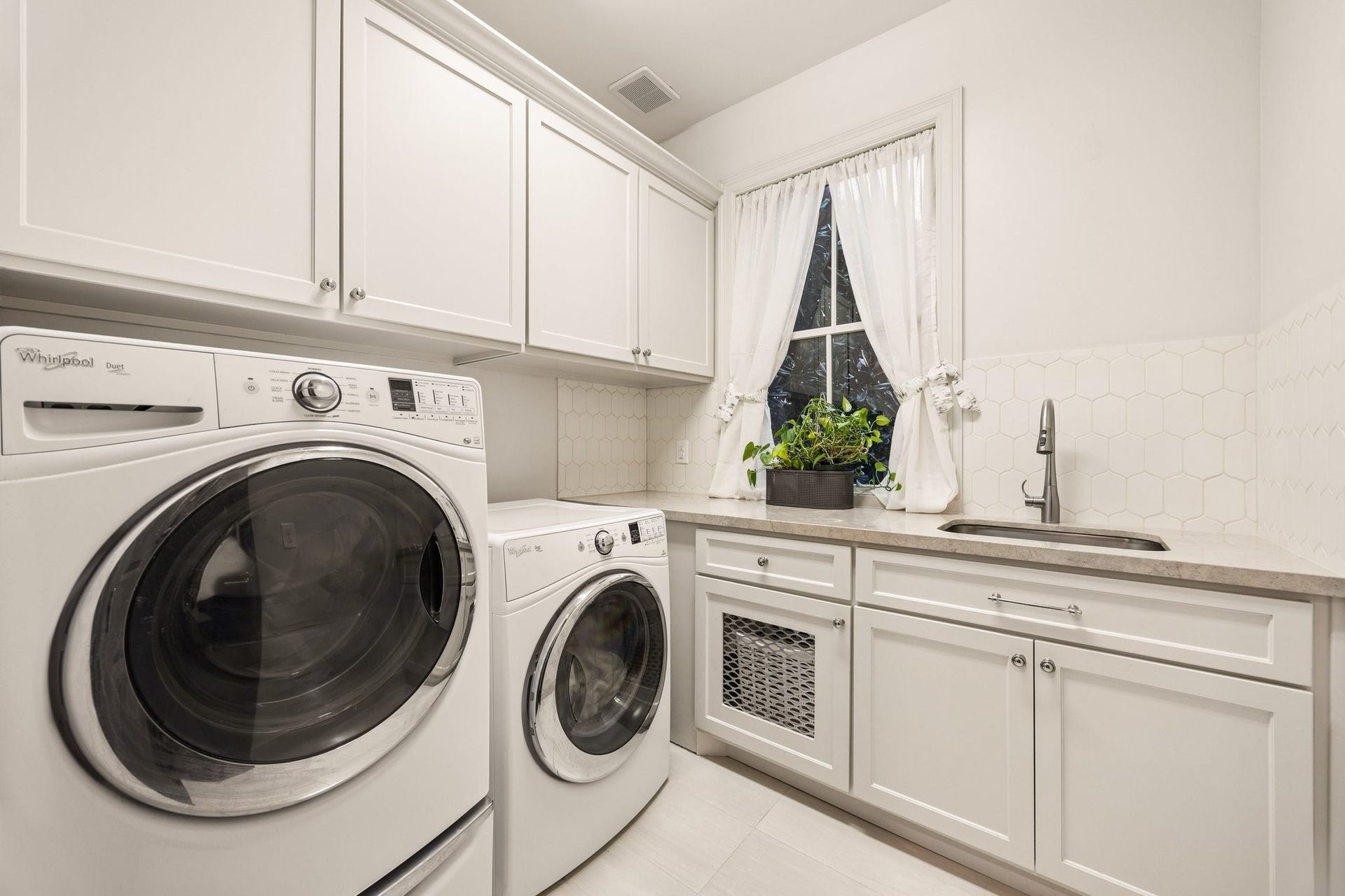 2131 Bancroft Street, Houston, TX 77027 Bright, beautifully appointed laundry room featuring Whirlpool washer and dryer, custom cabinetry, generous counter space, utility sink, and elegant tile backsplash.