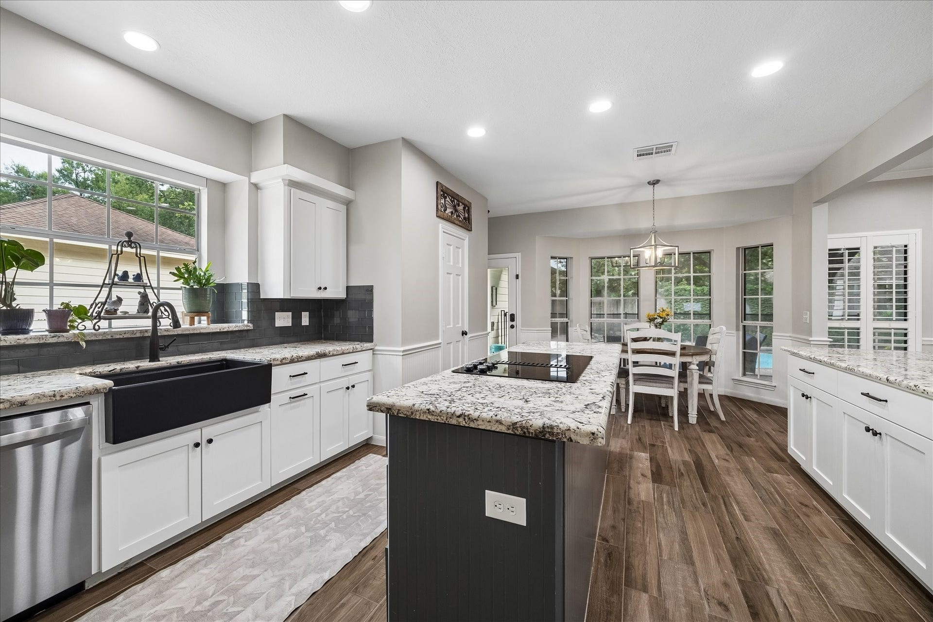 2411 Kings Lodge Drive, Kingwood, TX 77345 Elegant kitchen with granite countertops, a large farmhouse sink, and a spacious island. The open layout flows into a bright dining area with large windows, offering a view of the backyard.
