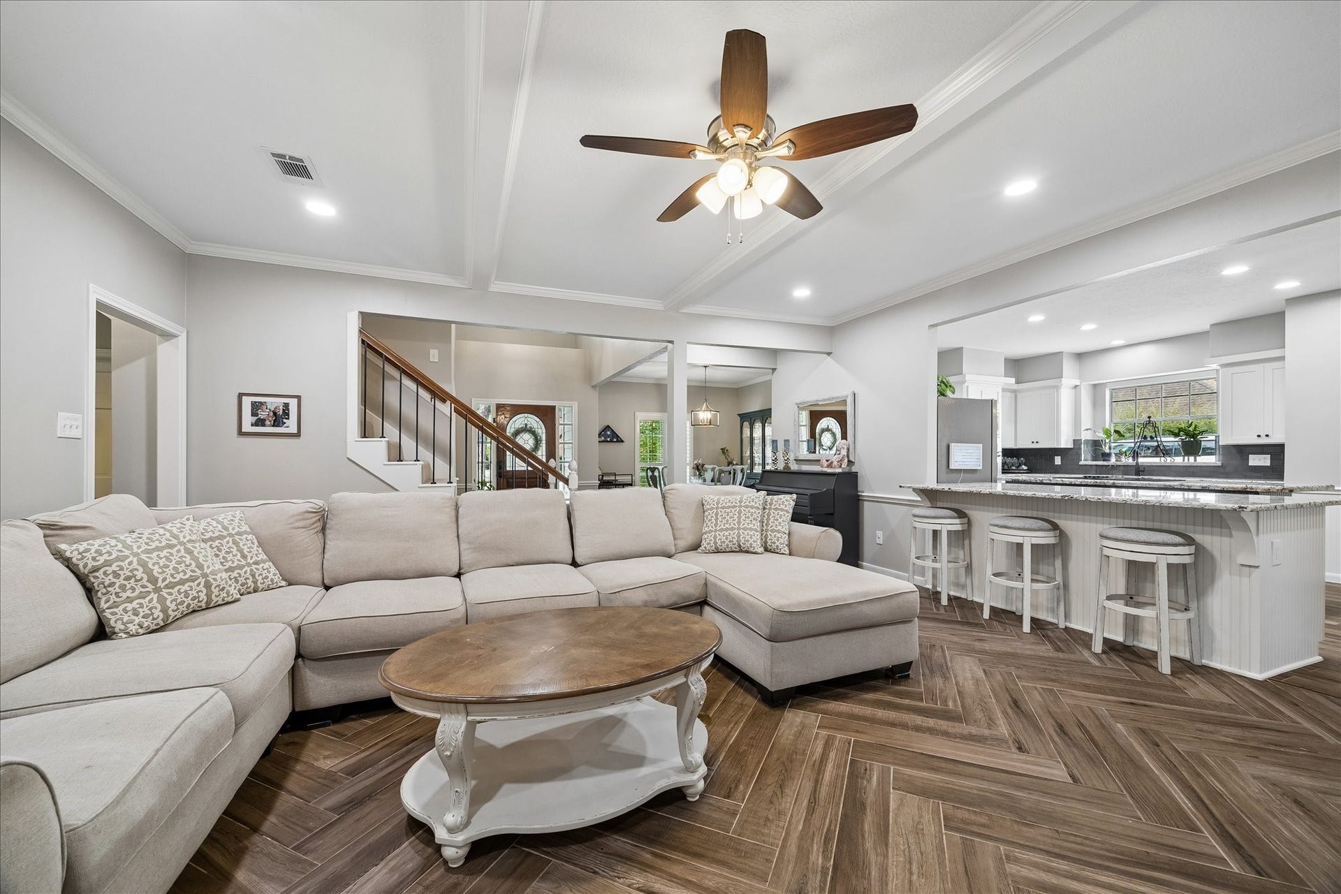 2411 Kings Lodge Drive, Kingwood, TX 77345 Spacious open-concept living area with elegant herringbone wood flooring, a cozy sectional sofa, and a modern kitchen featuring a large island and bar seating.
