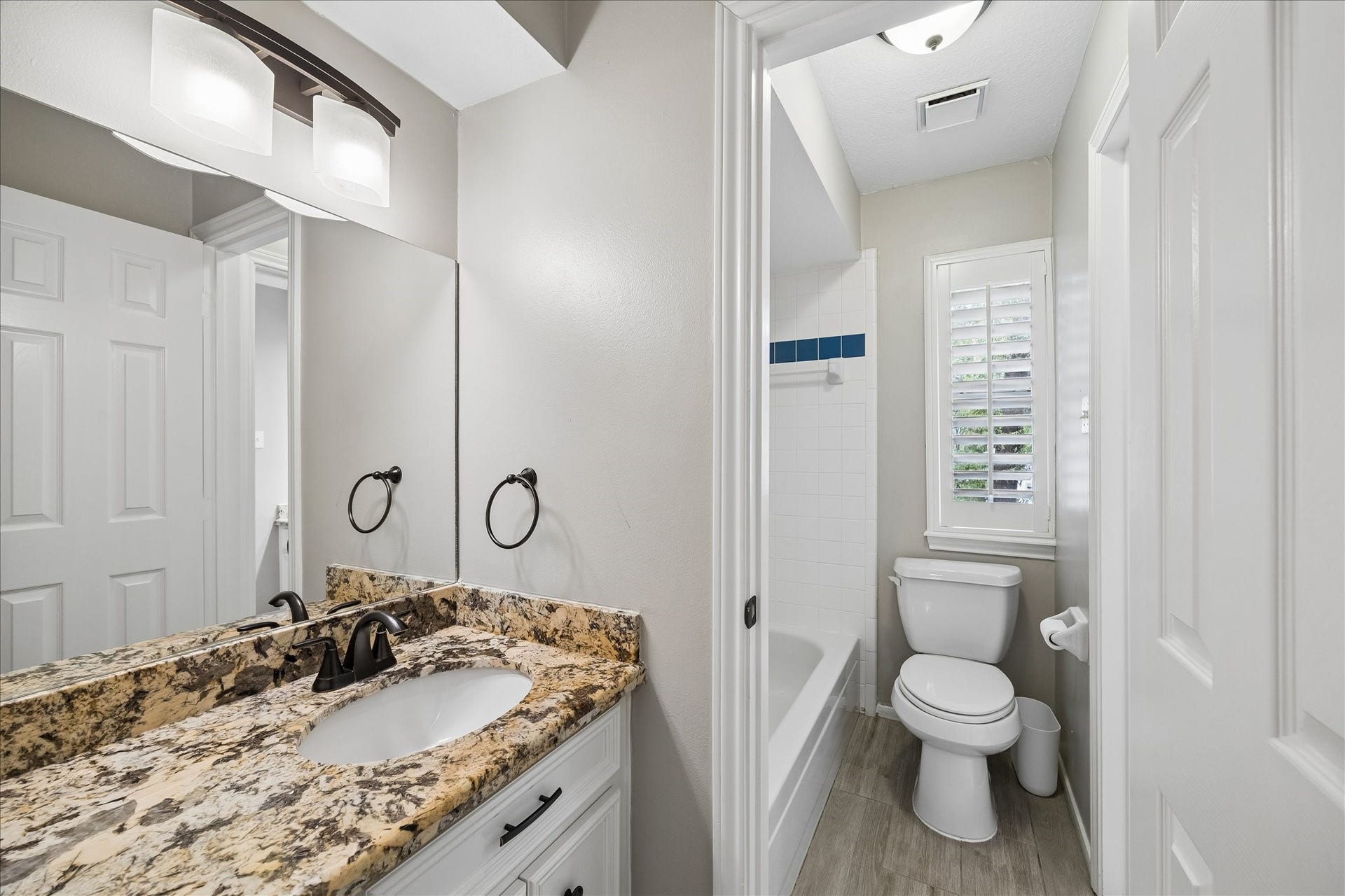 2411 Kings Lodge Drive, Kingwood, TX 77345 Full bathroom off of the gameroom, featuring a granite countertop, modern fixtures, and a bright window with shutters, complementing the elegant tile flooring and classic tub-shower combination.