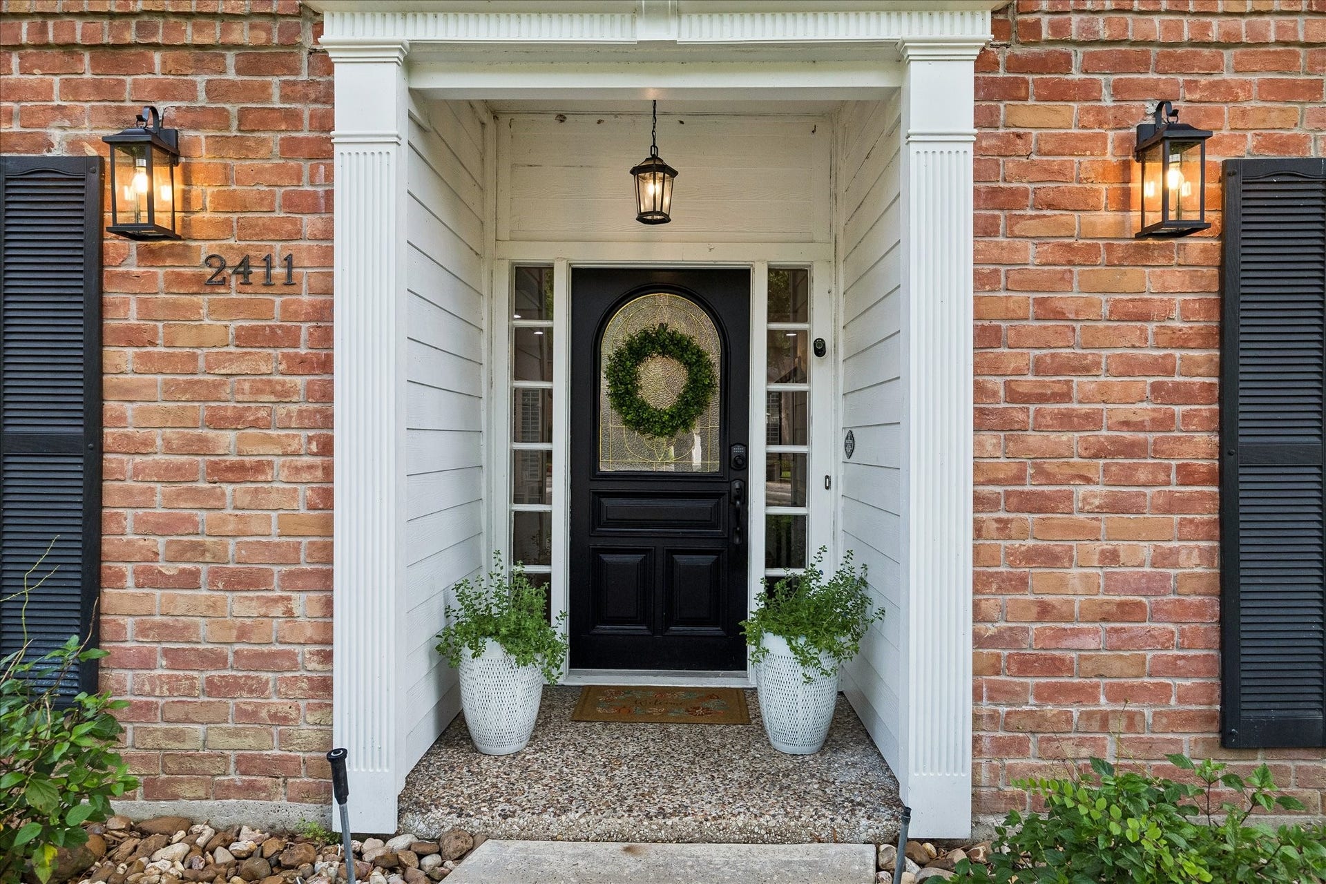 2411 Kings Lodge Drive, Kingwood, TX 77345 Charming entrance with classic brickwork, elegant black door, and inviting greenery, enhanced by warm exterior lighting.