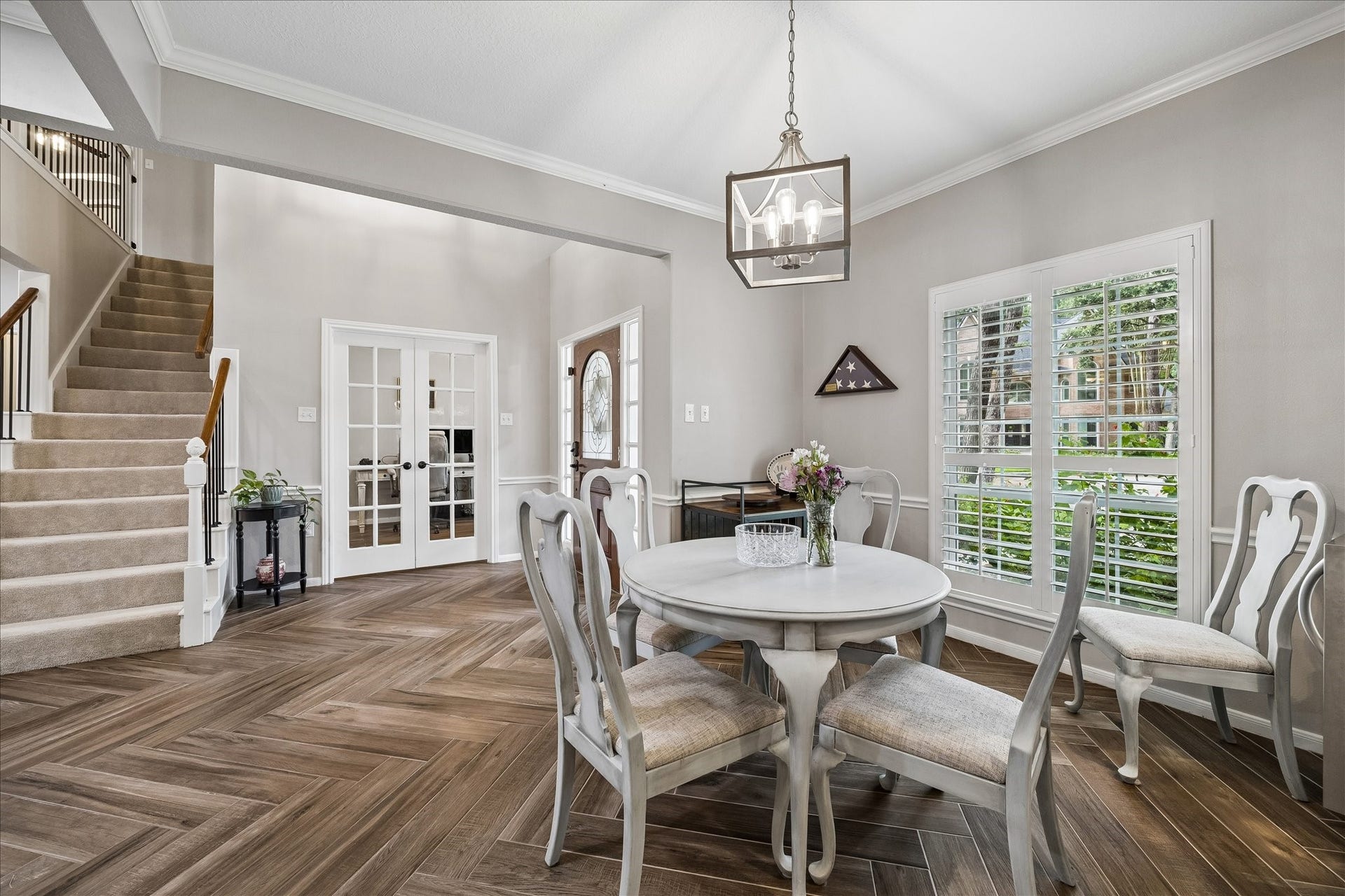 2411 Kings Lodge Drive, Kingwood, TX 77345 Elegant dining area with herringbone ceramic wood flooring. Natural light pours in through large windows with plantation shutters, highlighting the open space leading to a staircase and French doors.