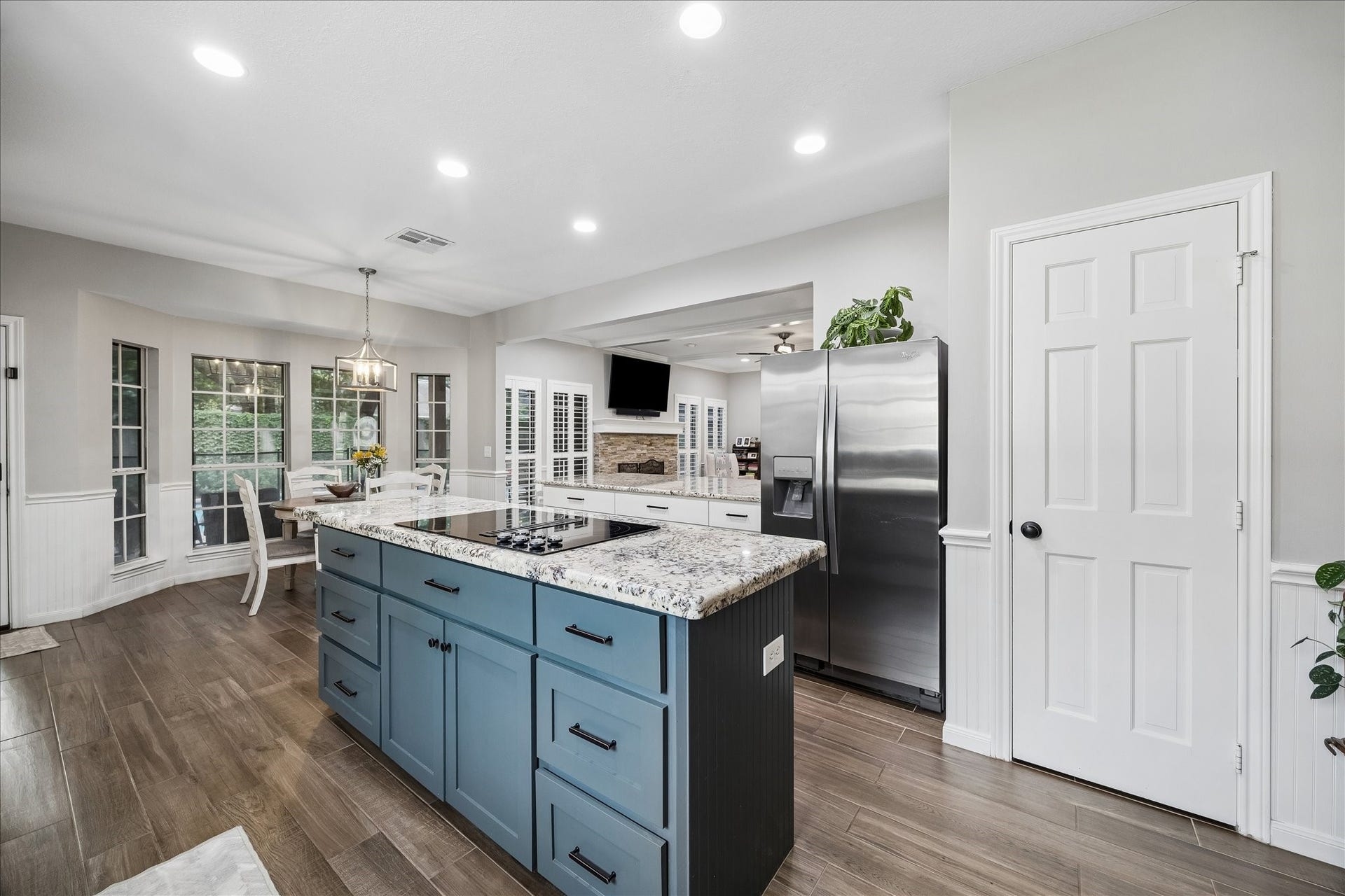 2411 Kings Lodge Drive, Kingwood, TX 77345 Spacious kitchen featuring a large granite island with a cooktop, modern stainless steel appliances, and elegant wood flooring, seamlessly connecting to a bright dining area with ample natural light.