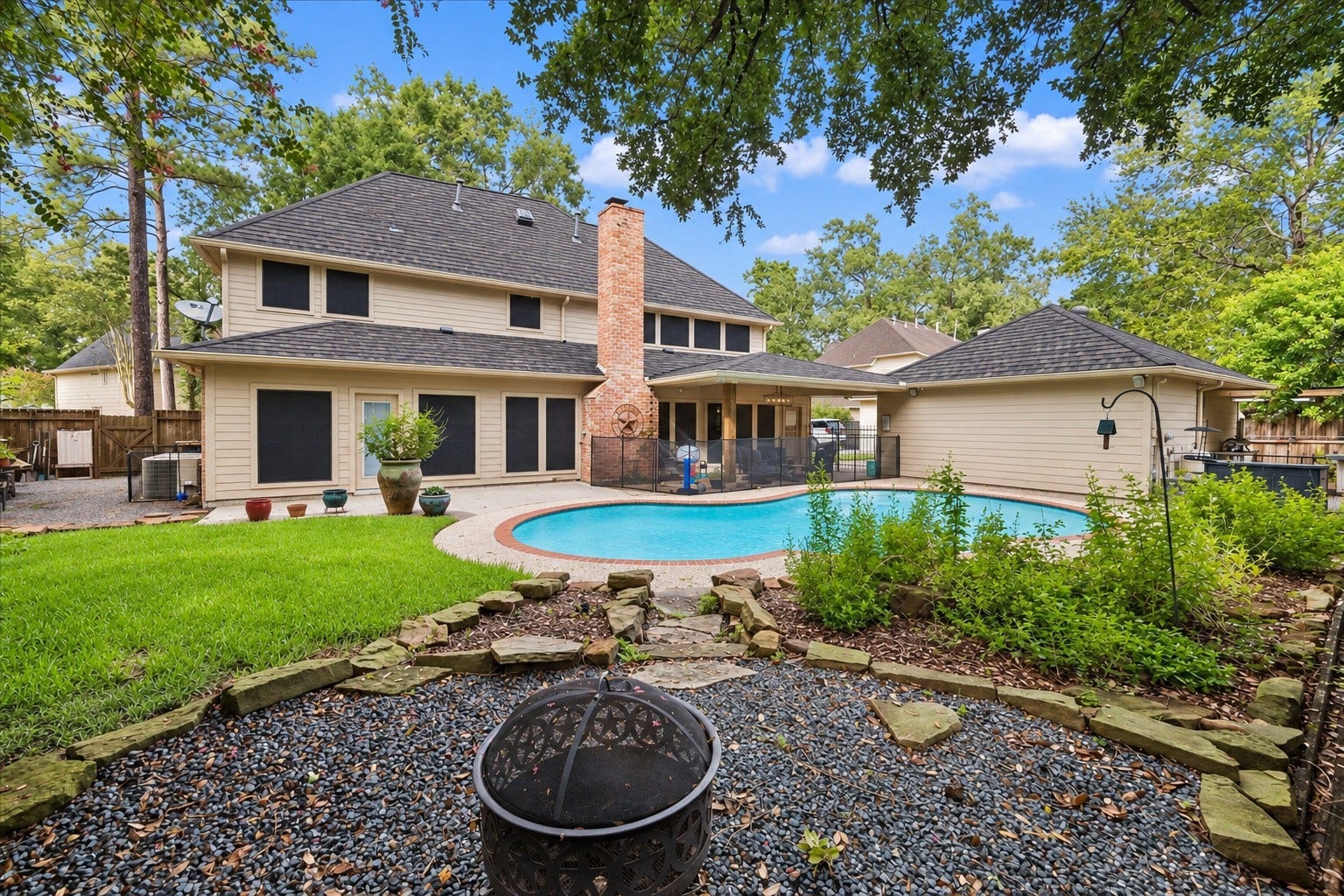 2411 Kings Lodge Drive, Kingwood, TX 77345 Spacious backyard retreat featuring a sparkling pool, lush greenery, and charming stone accents, perfect for relaxation and entertaining. Newly installed and removable safety fencing.