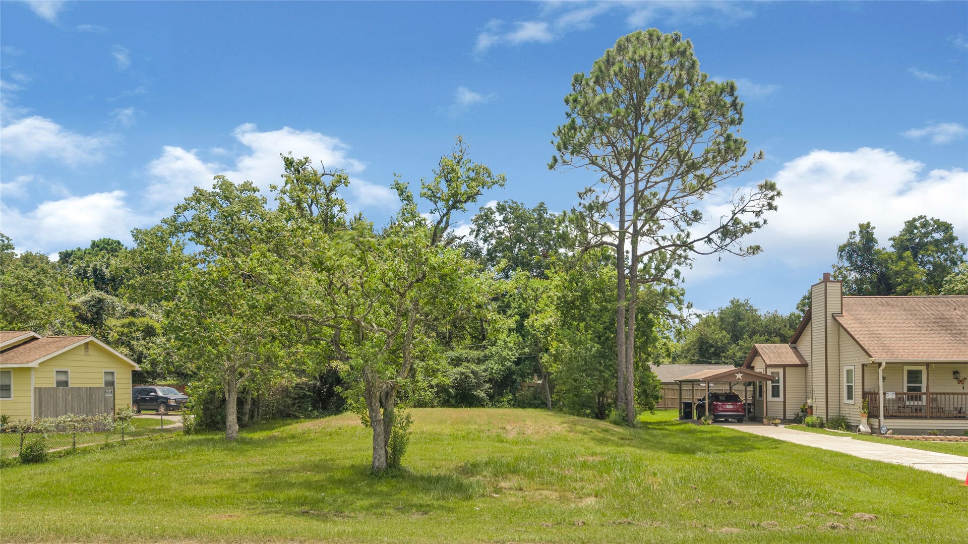6519 Pinecrest Drive, Hitchcock, TX 77563 Spacious lot nestled between charming homes, featuring mature trees and a lush, green lawn, perfect for building your dream home in a serene neighborhood.
