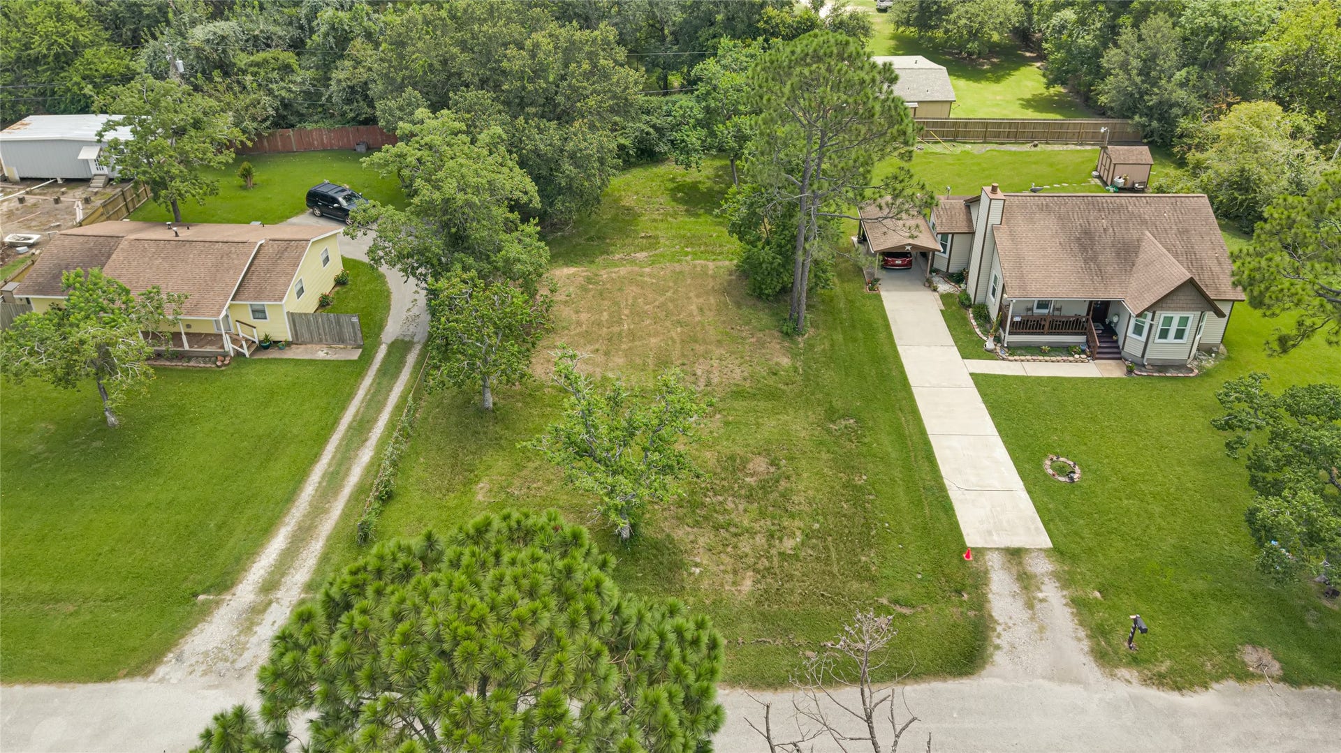 6519 Pinecrest Drive, Hitchcock, TX 77563 Spacious lot with lush greenery and mature trees, featuring two charming homes with ample yard space and long driveways, perfect for privacy and outdoor activities.