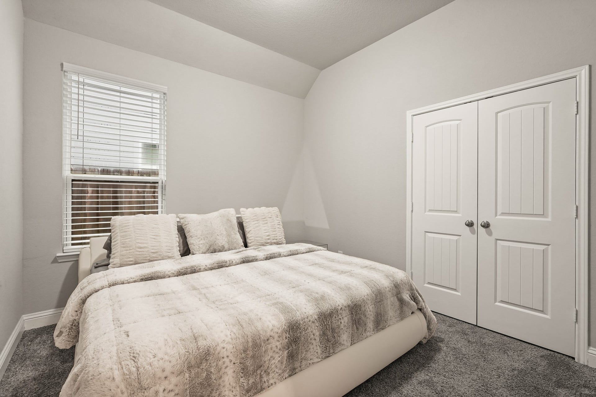 1710 Forest Mist Drive, Missouri City, TX 77459 This inviting bedroom features deep grey carpeting for a warm, comfortable atmosphere. A large window with built-in blinds provides excellent natural light, while the vaulted ceiling detail adds architectural interest and vertical space. Double closet doors with classic raised panel details complete the room, offering ample storage space.