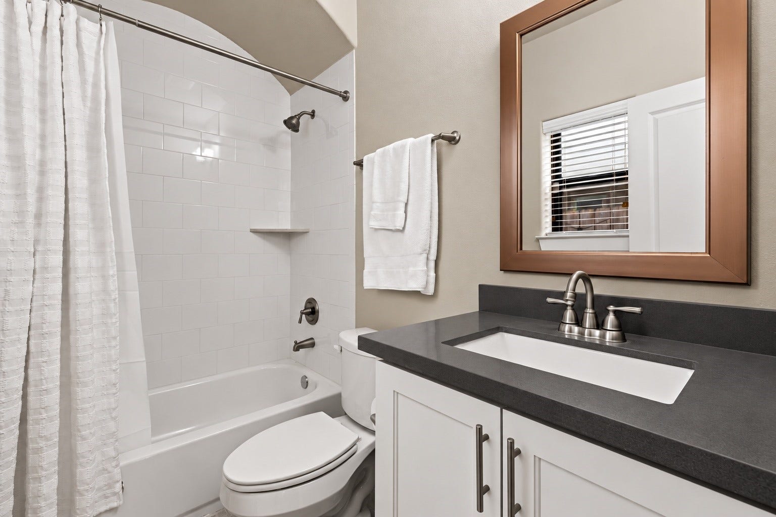 868 Wakefield Drive, #B, Houston, TX 77018 A dark vanity counter strikes a refined contrast against white cabinetry and pale walls. The adjoining tub-and-shower combination completes a comfortable full bath.