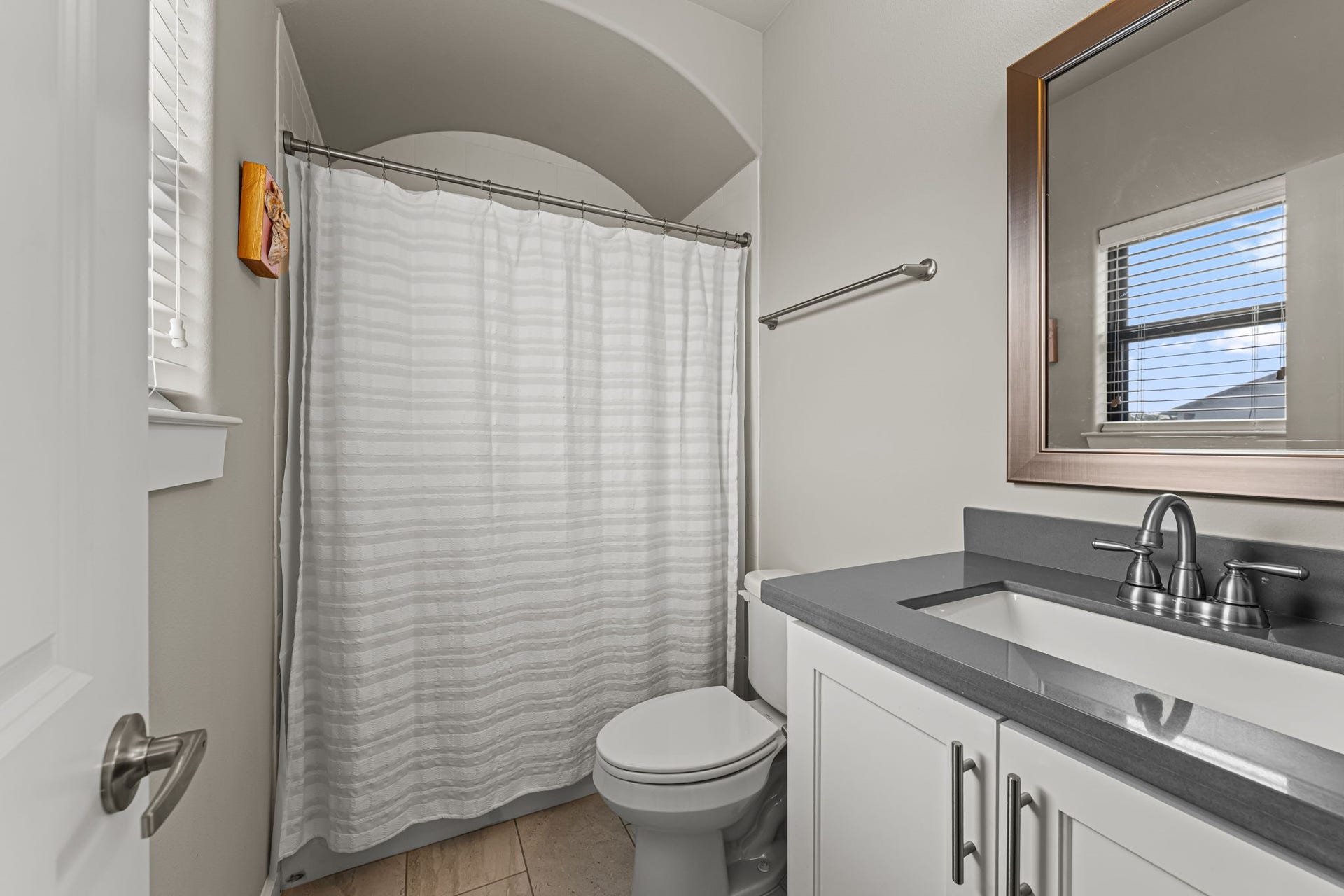 868 Wakefield Drive, #B, Houston, TX 77018 An arched opening frames the tub-and-shower area with a graceful architectural flourish. A dark vanity counter and nearby window balance rich contrast with natural light.
