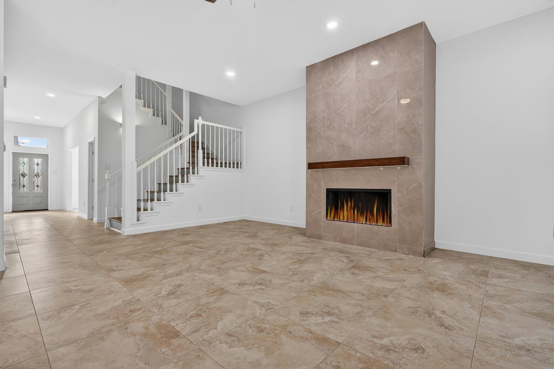 4720 Post Oak Timber Drive, #23, Houston, TX 77056 Spacious open-concept living room featuring soaring ceilings, oversized tile flooring, recessed lighting, and a stunning floor-to-ceiling tiled fireplace with modern wood mantle. Elegant staircase with wood accents creates a grand focal point, while the bright neutral finishes make this home move-in ready and perfect for entertaining.