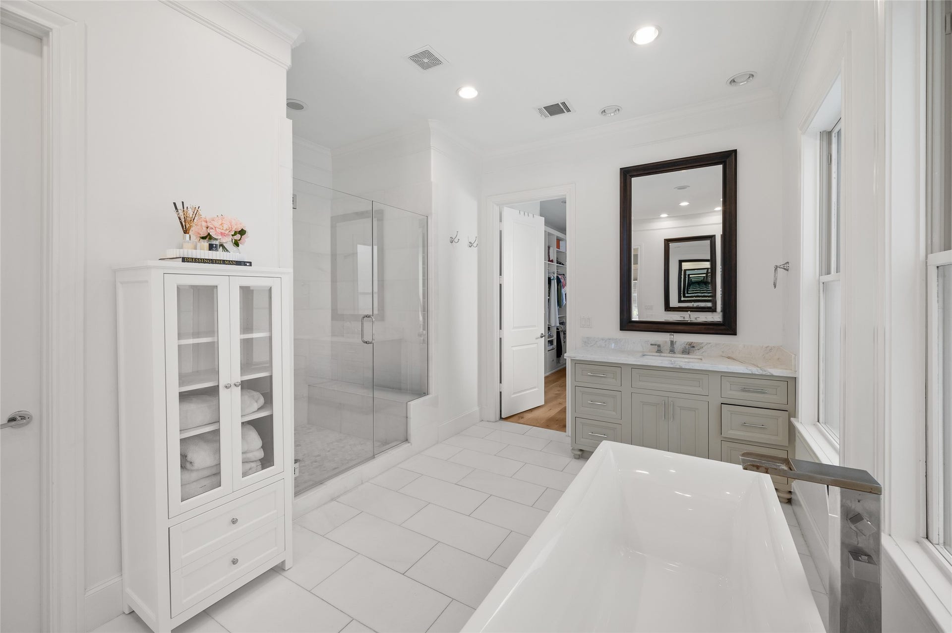 7554 Little Caprese Lane, Houston, TX 77055 Freestanding soaking tub positioned beneath three windows, with marble-topped vanity and elegant white tile flooring.