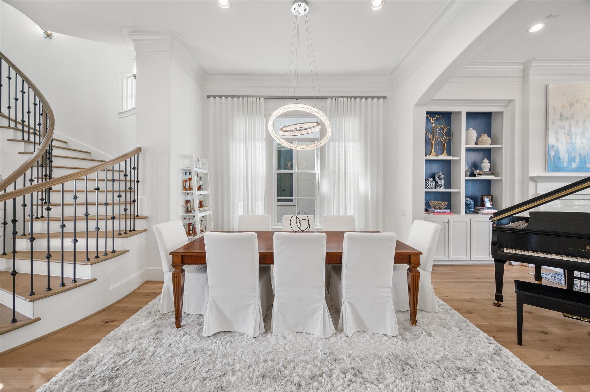 7554 Little Caprese Lane, Houston, TX 77055 Formal dining room anchored by a sculptural ring chandelier, with wide-plank oak floors, tailored millwork, and custom built-ins beyond.
