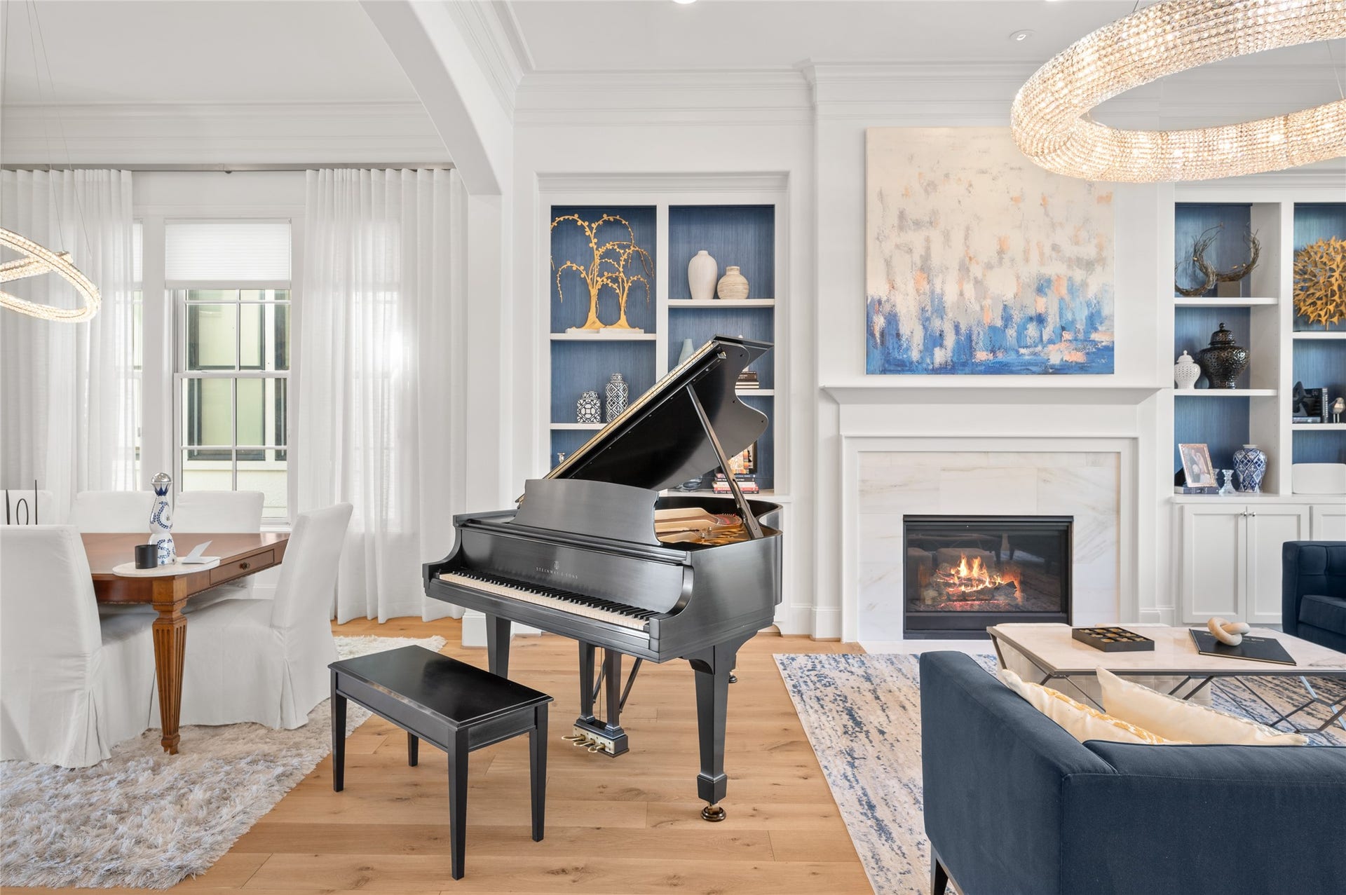7554 Little Caprese Lane, Houston, TX 77055 A striking Steinway grand piano complements the home's interconnected living and dining spaces, framed by custom blue-accented built-ins and a marble-surround fireplace.