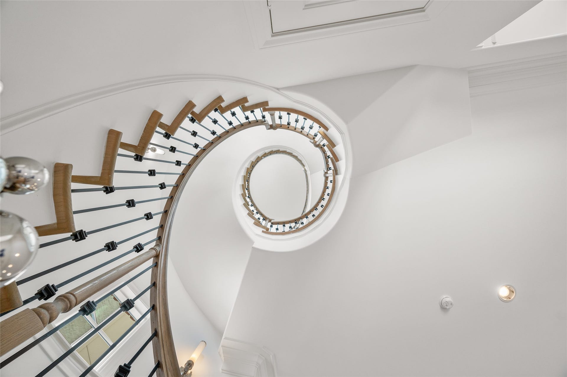 7554 Little Caprese Lane, Houston, TX 77055 Striking curved staircase featuring natural wood treads, wrought-iron balusters, and a sculptural design spanning multiple levels.