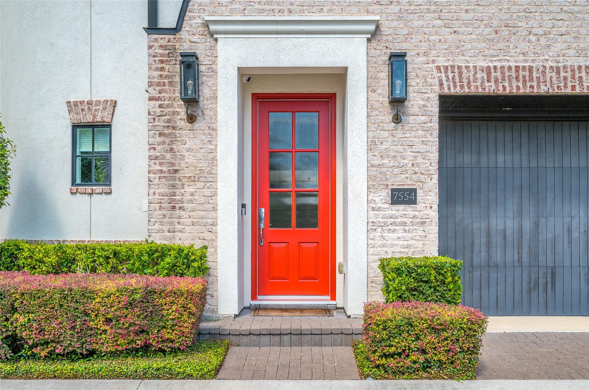 7554 Little Caprese Lane, Houston, TX 77055 A striking red entry door makes a memorable first impression, framed by gorgeous brickwork, classic lantern-style sconces, and meticulously manicured landscaping.