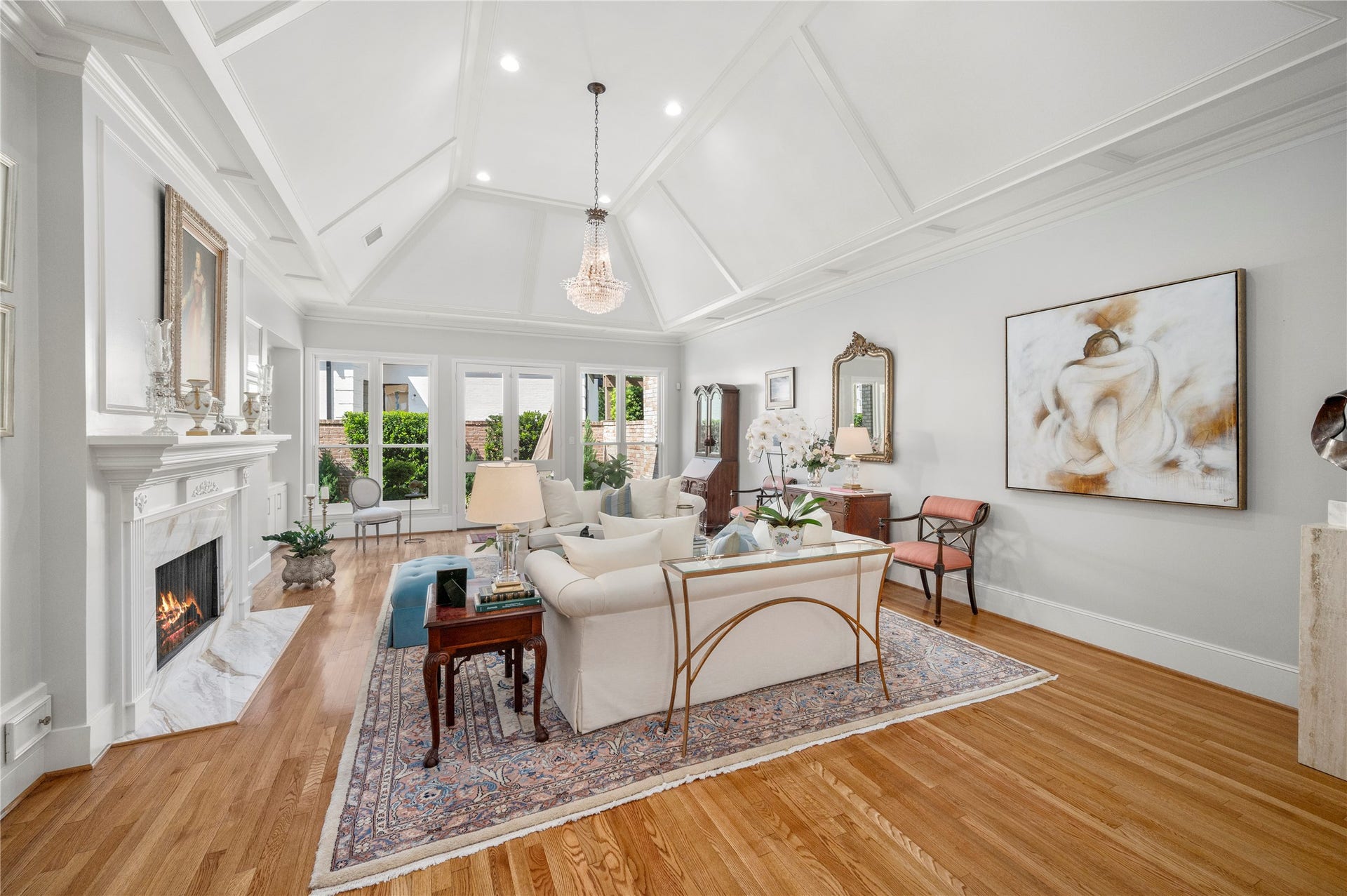 [Living Room]
Light-filled living room features a fireplace with marble surround, a soaring cathedral ceiling, and a rear wall of glass doors and full-length windows overlooking the patio.