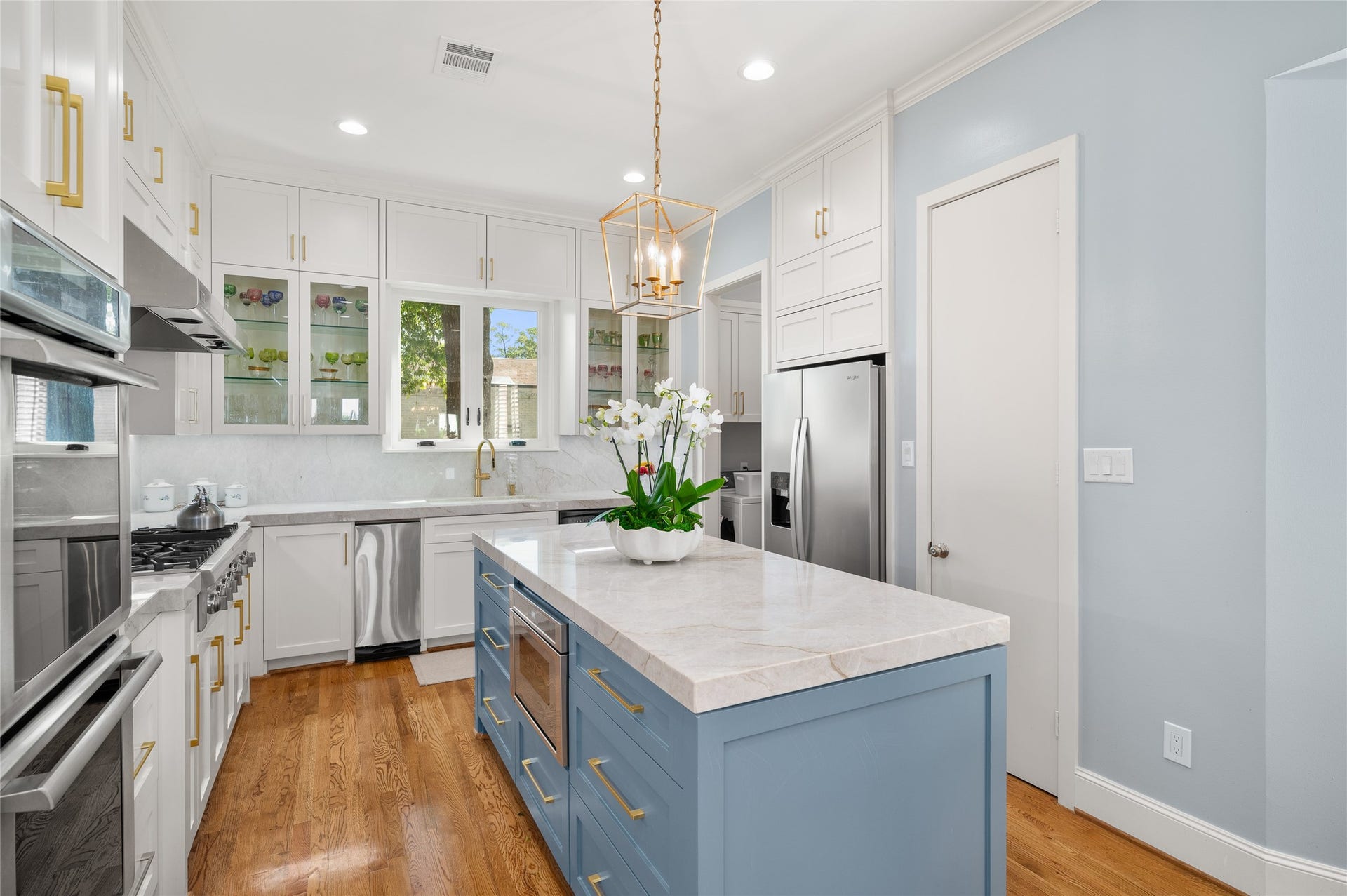 [Gathering Kitchen]
A closer view reveals the center island and lighted, glass-faced jumper cabinets flanking the deep sink and gooseneck faucet.