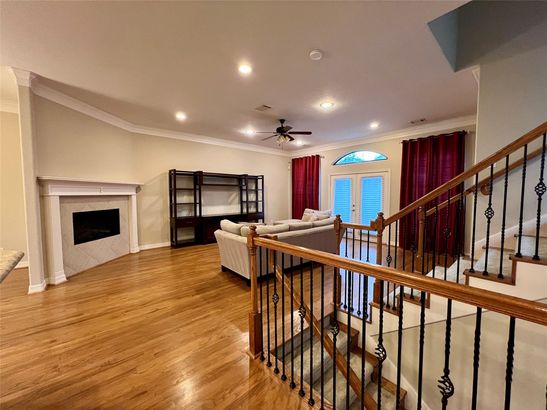 1625 Cohn Street, Houston, TX 77007 This spacious living room features hardwood flooring, a cozy fireplace, and ample natural light from large windows and glass doors. The room includes a built-in shelving unit and a comfortable seating area, with elegant iron and wood railing on the staircase for added style.