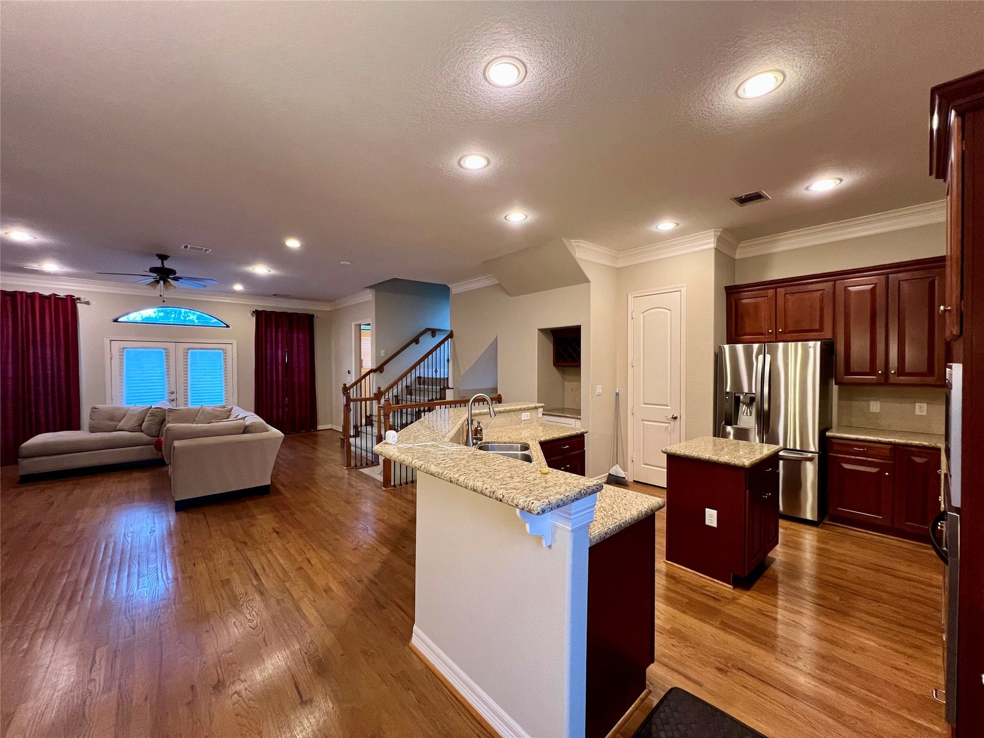 1625 Cohn Street, Houston, TX 77007 This open-concept living area features a spacious kitchen with granite countertops, stainless steel appliances, and rich wood cabinetry. The living room offers hardwood floors, a cozy sectional sofa, and ample natural light from large windows and glass doors. Perfect for entertaining and family living.