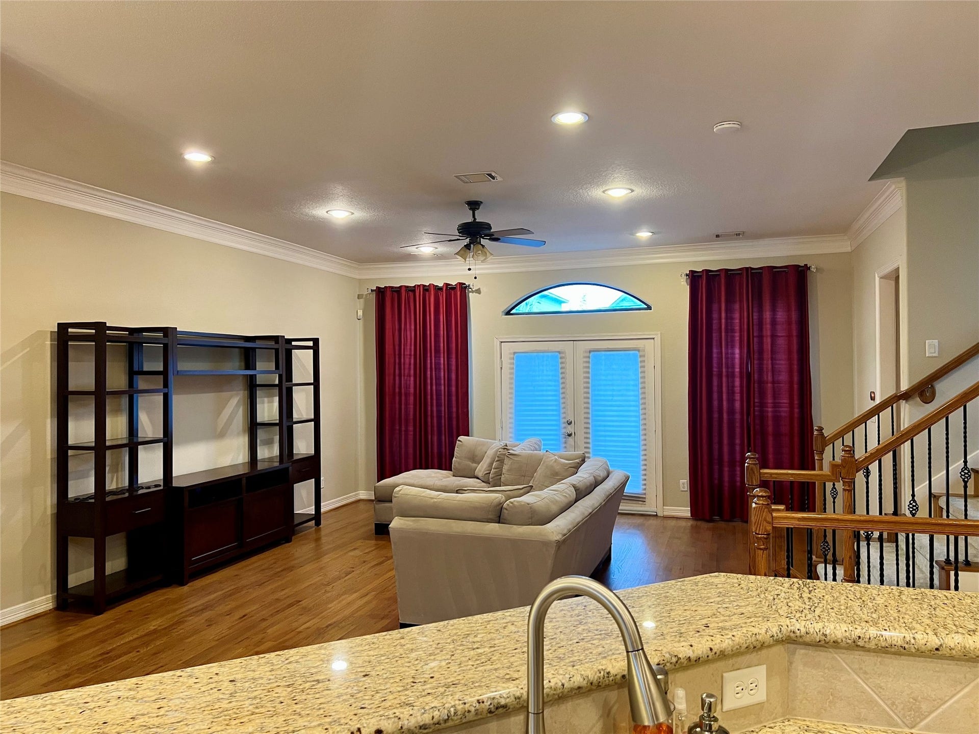 1625 Cohn Street, Houston, TX 77007 Spacious living room with hardwood floors, featuring a cozy sectional sofa and a large entertainment unit. The room is well-lit with recessed lighting and a ceiling fan. French doors with red curtains lead outside