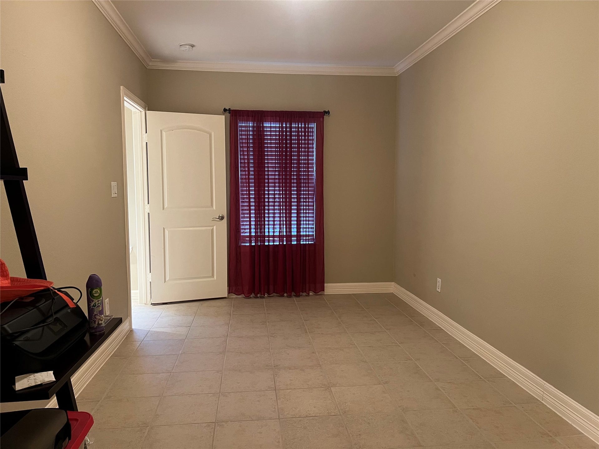 1625 Cohn Street, Houston, TX 77007 This room features neutral walls, tiled flooring, and a window with red curtains allowing natural light. It has a white door and crown molding, providing a clean and simple space.