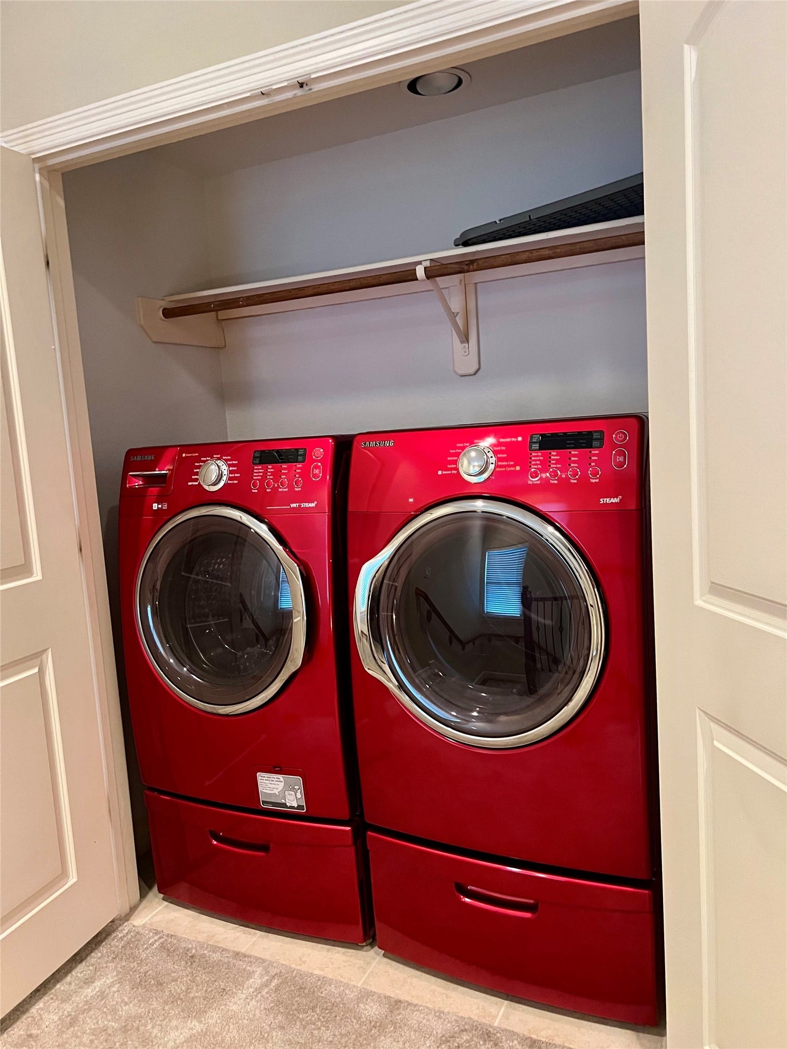 1625 Cohn Street, Houston, TX 77007 A laundry closet with a vibrant red front-loading washer and dryer set. There's a shelf above for storage, and the area is neatly enclosed by doors.