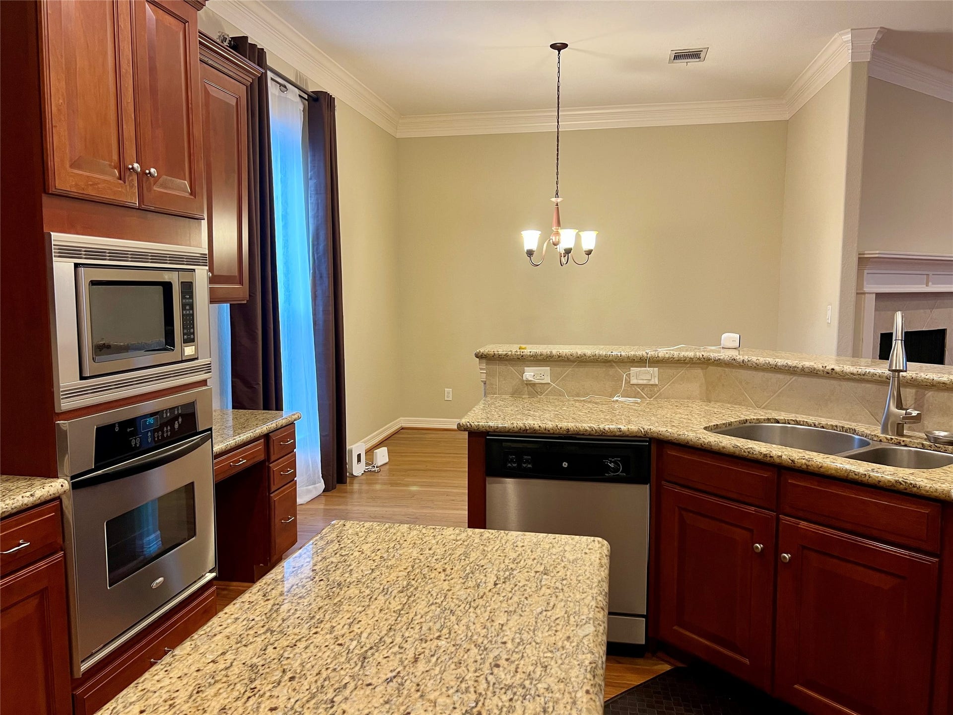 1625 Cohn Street, Houston, TX 77007 This kitchen features elegant granite countertops, stainless steel appliances, and rich wooden cabinetry. Its open layout, with a bar counter, overlooks a cozy dining area, enhanced by a stylish chandelier.