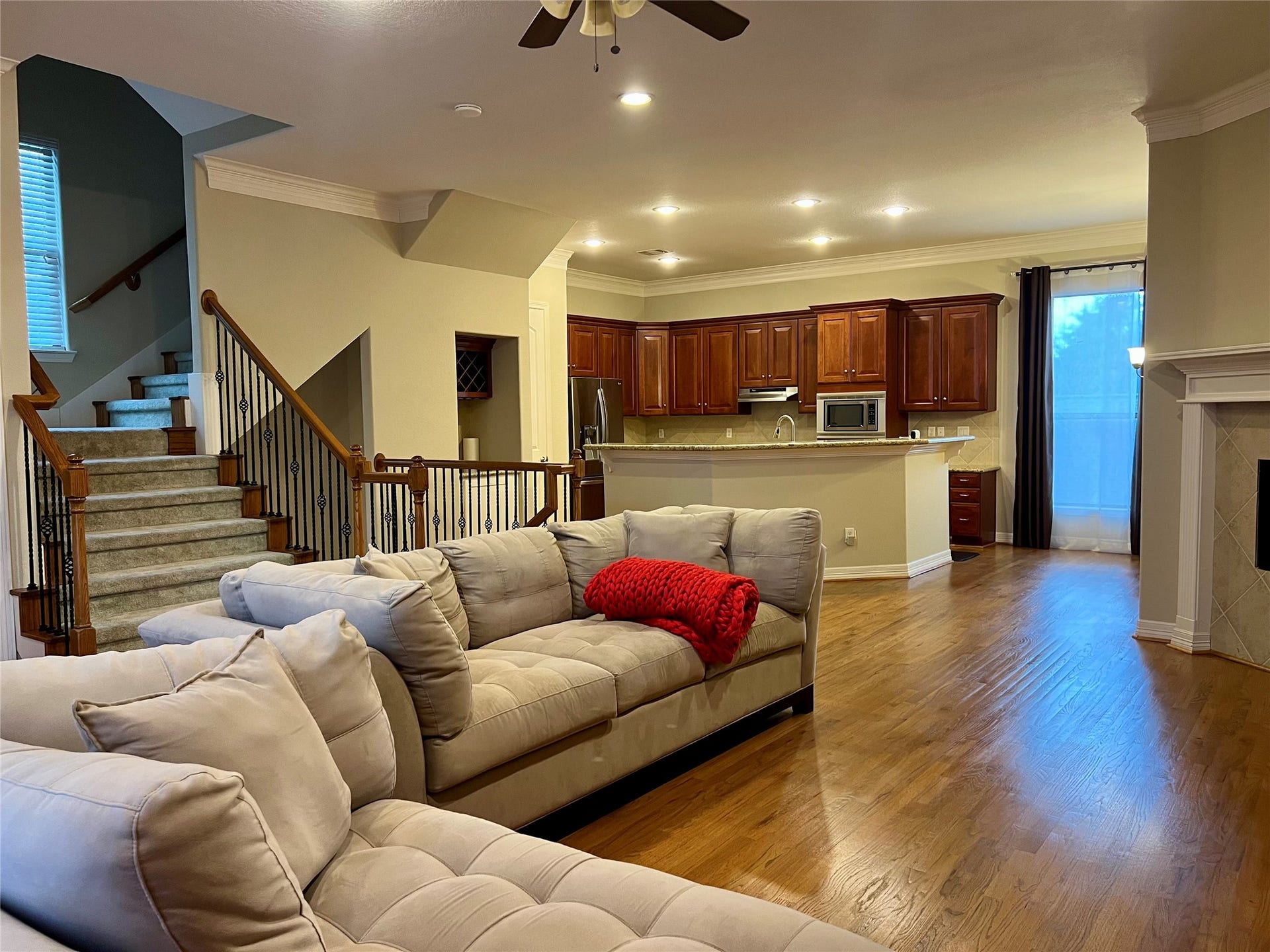 1625 Cohn Street, Houston, TX 77007 This inviting open-concept living space features hardwood floors, a cozy fireplace, and a modern kitchen with rich wood cabinetry and stainless steel appliances. The living area includes comfortable seating and access to a staircase, creating a warm and functional environment for family gatherings.
