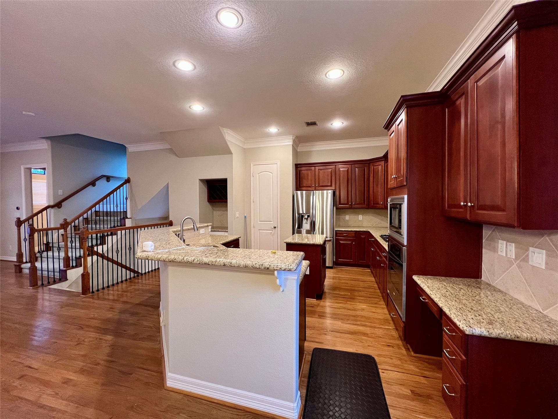 1625 Cohn Street, Houston, TX 77007 A spacious kitchen with rich wooden cabinets, granite countertops, and stainless steel appliances. The open layout connects to a staircase with elegant wooden railings, enhancing the home's warmth and functionality.