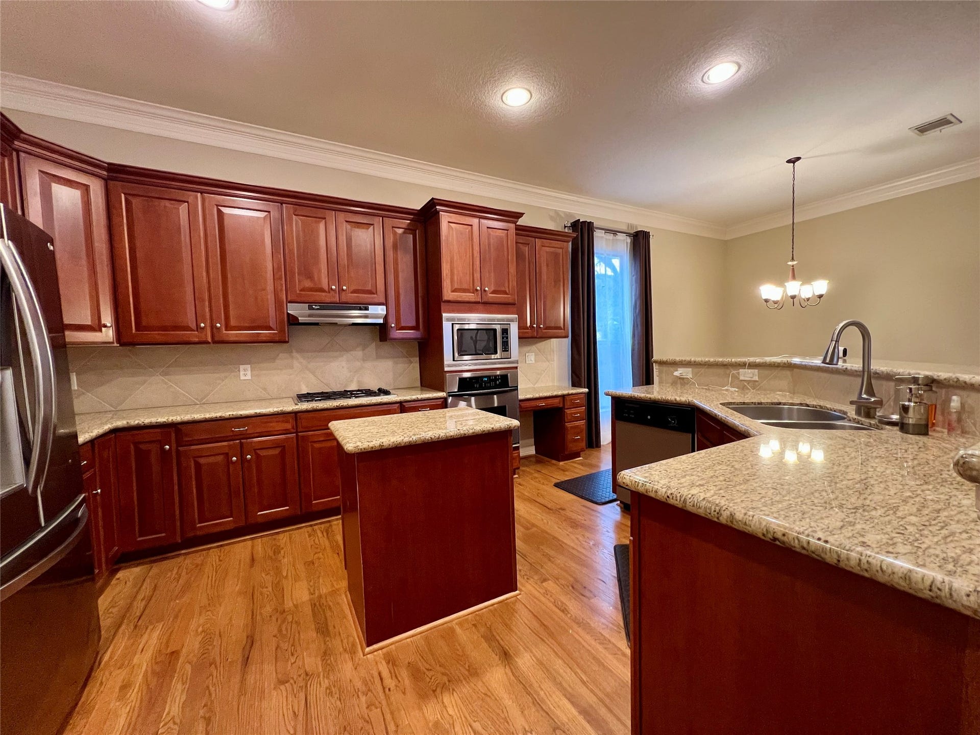 1625 Cohn Street, Houston, TX 77007 This kitchen features rich wood cabinetry, granite countertops, and hardwood floors. It includes stainless steel appliances, an island, and a modern light fixture, creating a warm and functional cooking space.