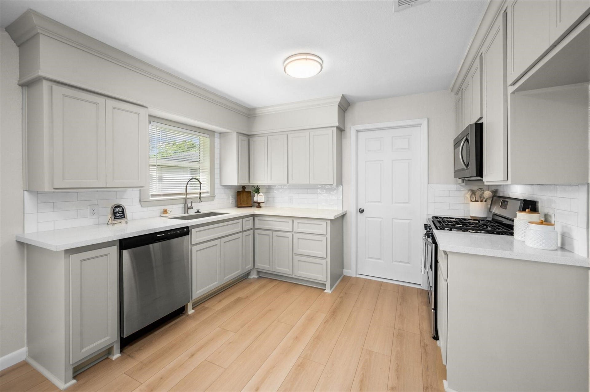 Bright and modern kitchen featuring sleek gray cabinetry, stainless steel appliances, and light wood flooring, creating a warm and inviting atmosphere.