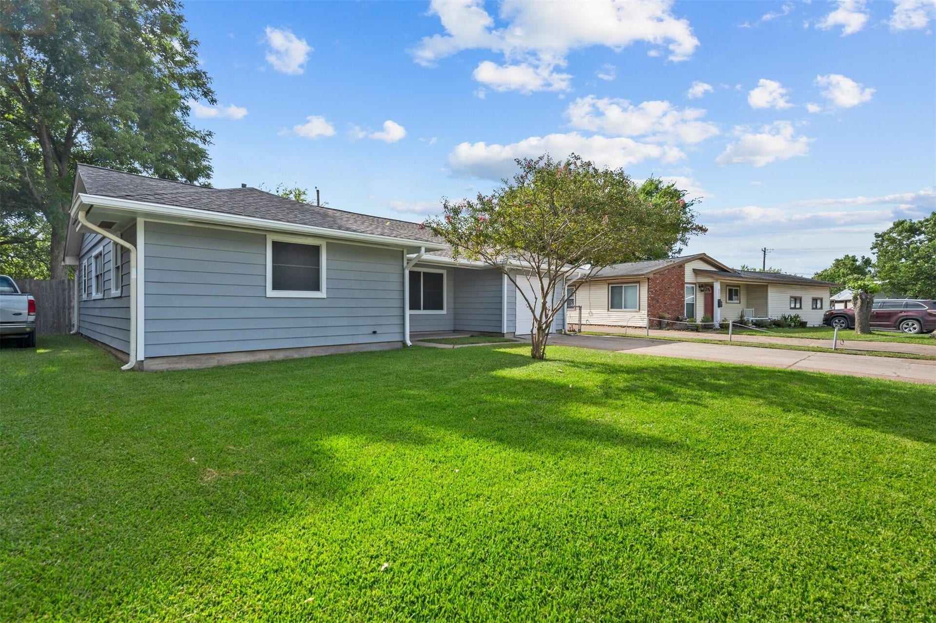 Charming single-story home with a spacious green lawn, mature trees, and a welcoming driveway, perfect for family living.