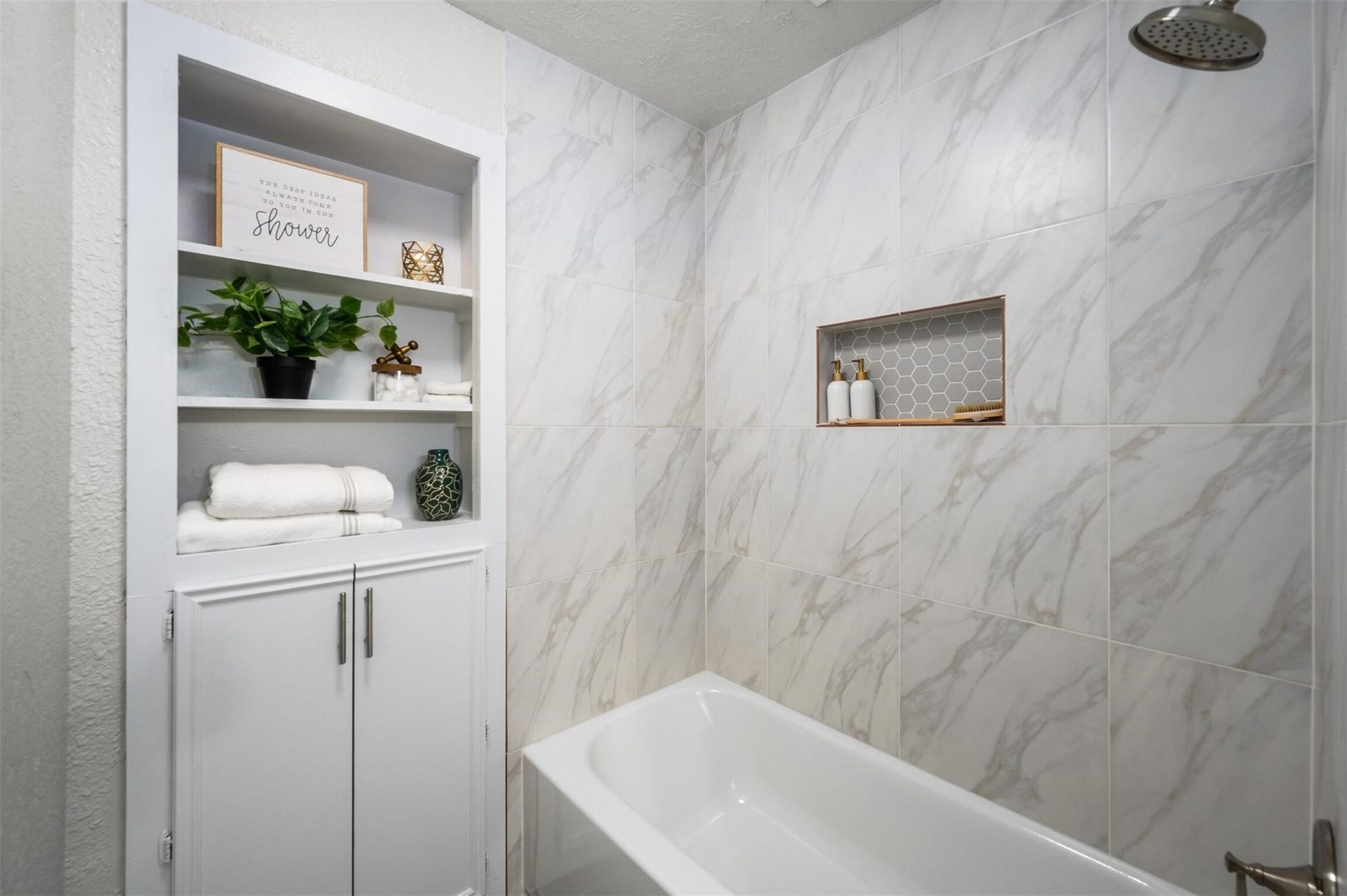 Elegant bathroom with sleek marble tile, a modern showerhead, and built-in shelving for stylish storage.