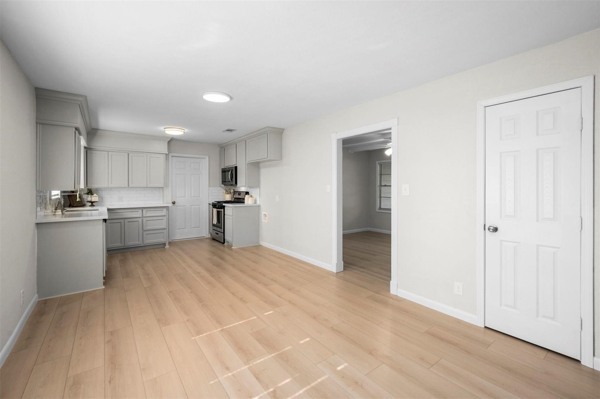 Discover a bright, open kitchen and dining area featuring sleek gray cabinetry, modern stainless steel appliances, and warm wood flooring, perfect for entertaining and daily living.