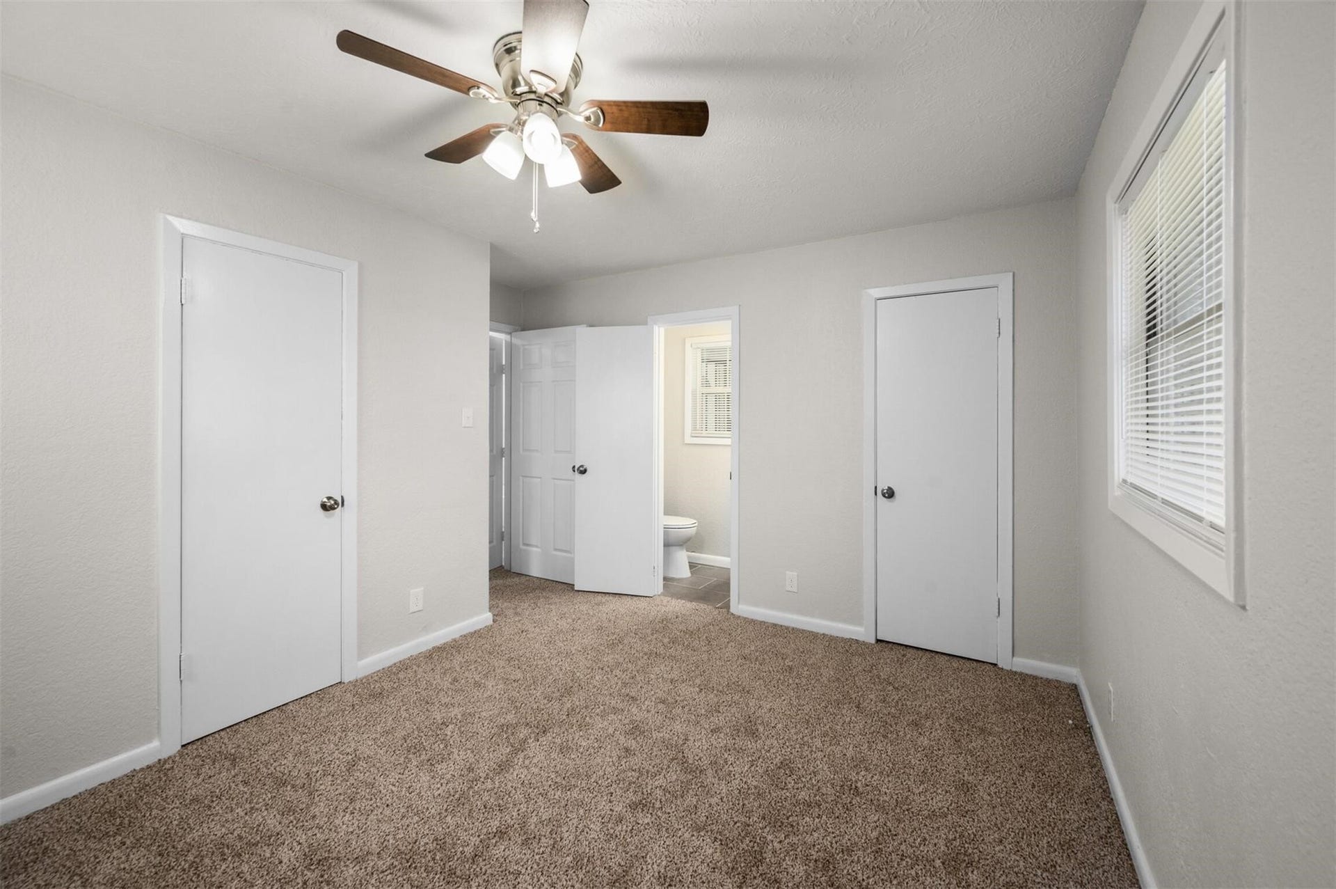 Bright bedroom with plush carpet, ceiling fan, and convenient en-suite bathroom access.
