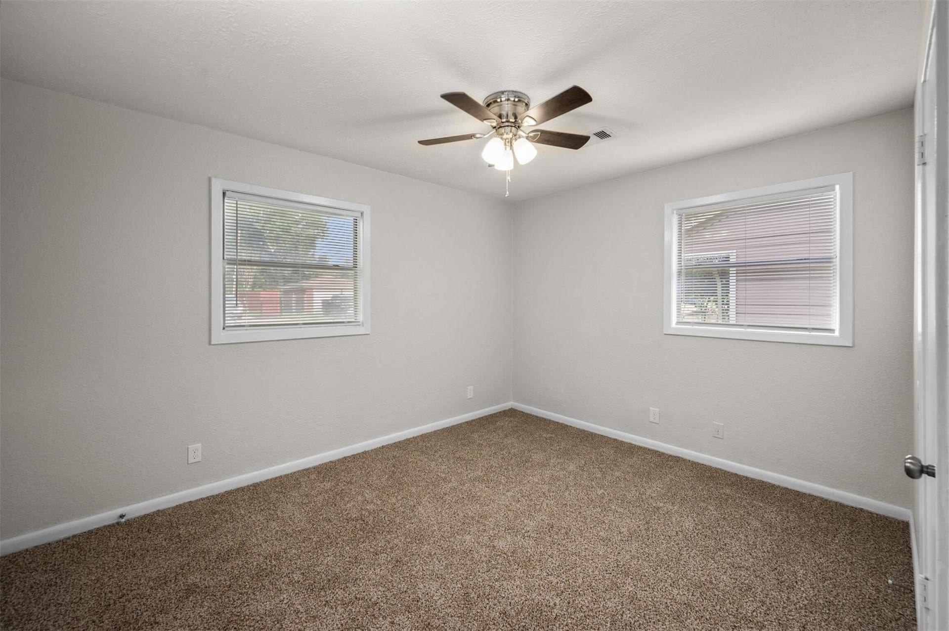 Cozy bedroom featuring soft carpet, neutral walls, and ample natural light from two windows, complemented by a stylish ceiling fan.
