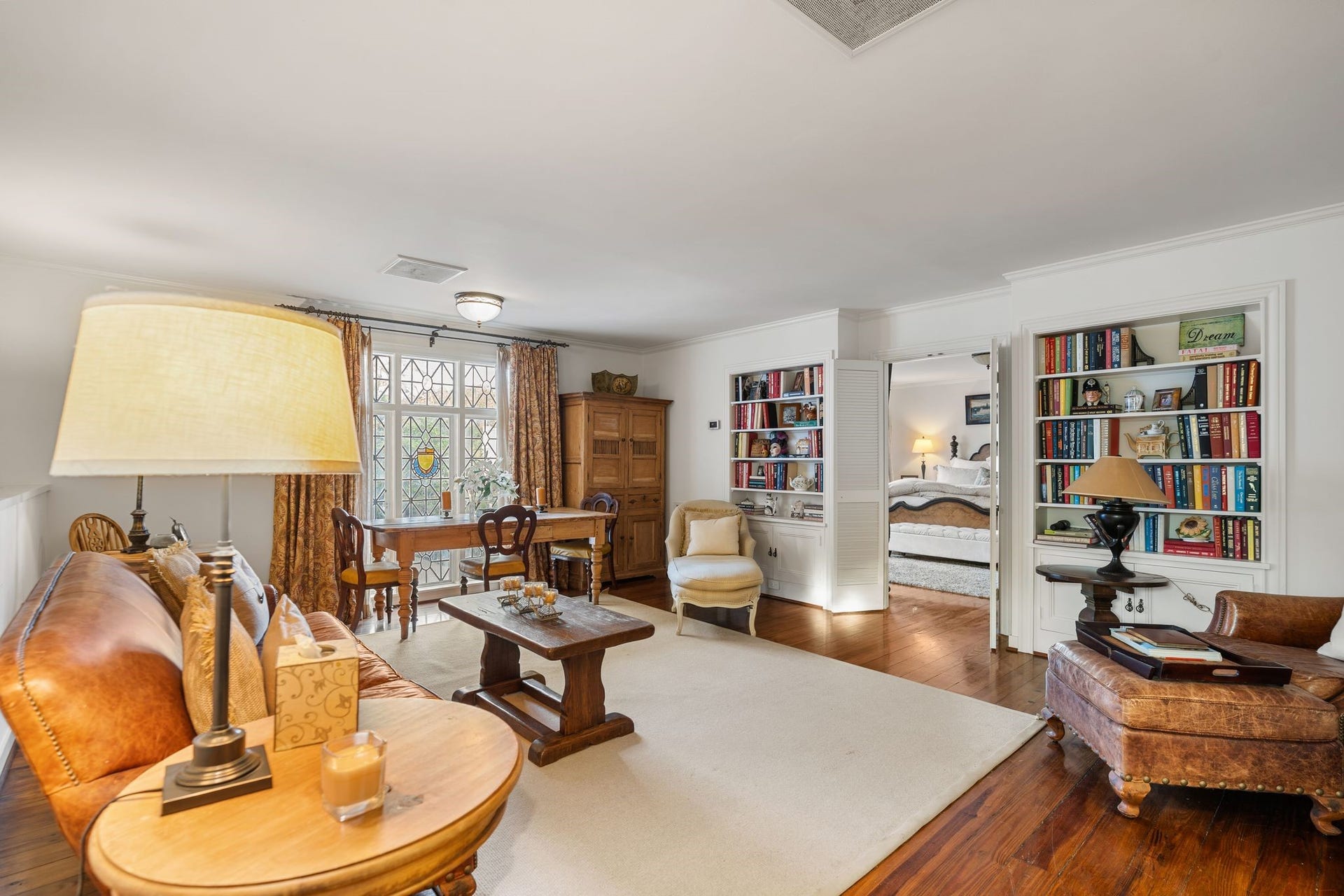 [Garage Apartment]
Above the three-car garage, this very large apartment is accessed by a staircase in the garage. The large living / dining area has a wide leaded and stained glass window that overlooks the driveway. Note book shelves and storage cabinets. Open louvered doors reveal the bedroom. Not shown; kitchenette with electric range, sink, under-counter refrigerator, and multiple step-in closets with louvered doors.