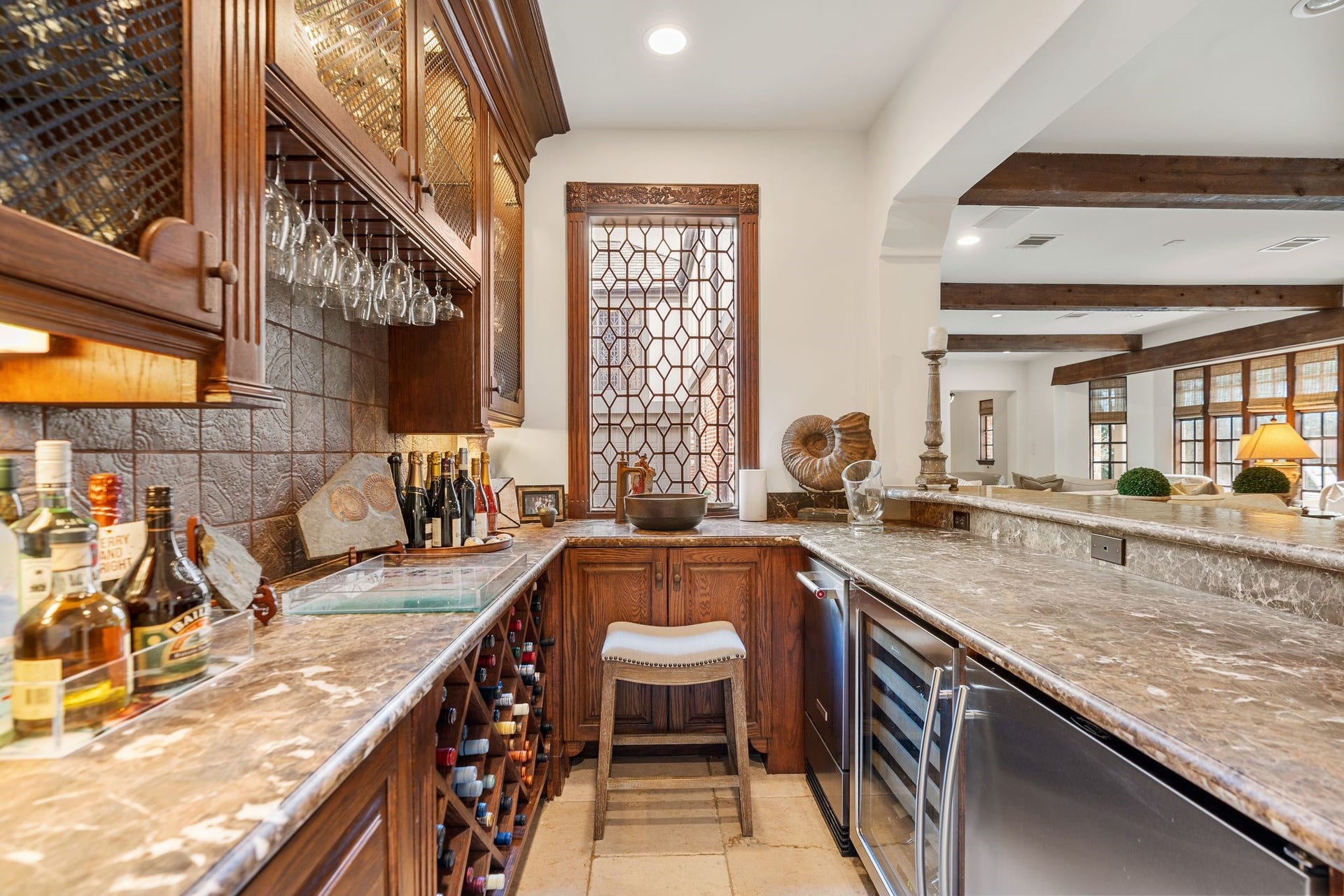 [Full Bar]
Wonderful full bar features stone countertops, embossed tile backsplash, a wine rack, wine chiller, and under-counter refrigerator. Illuminated jumper cabinets have wire mesh fronts. Leaded glass window at rear views the driveway, motor court, and 3-car garage.