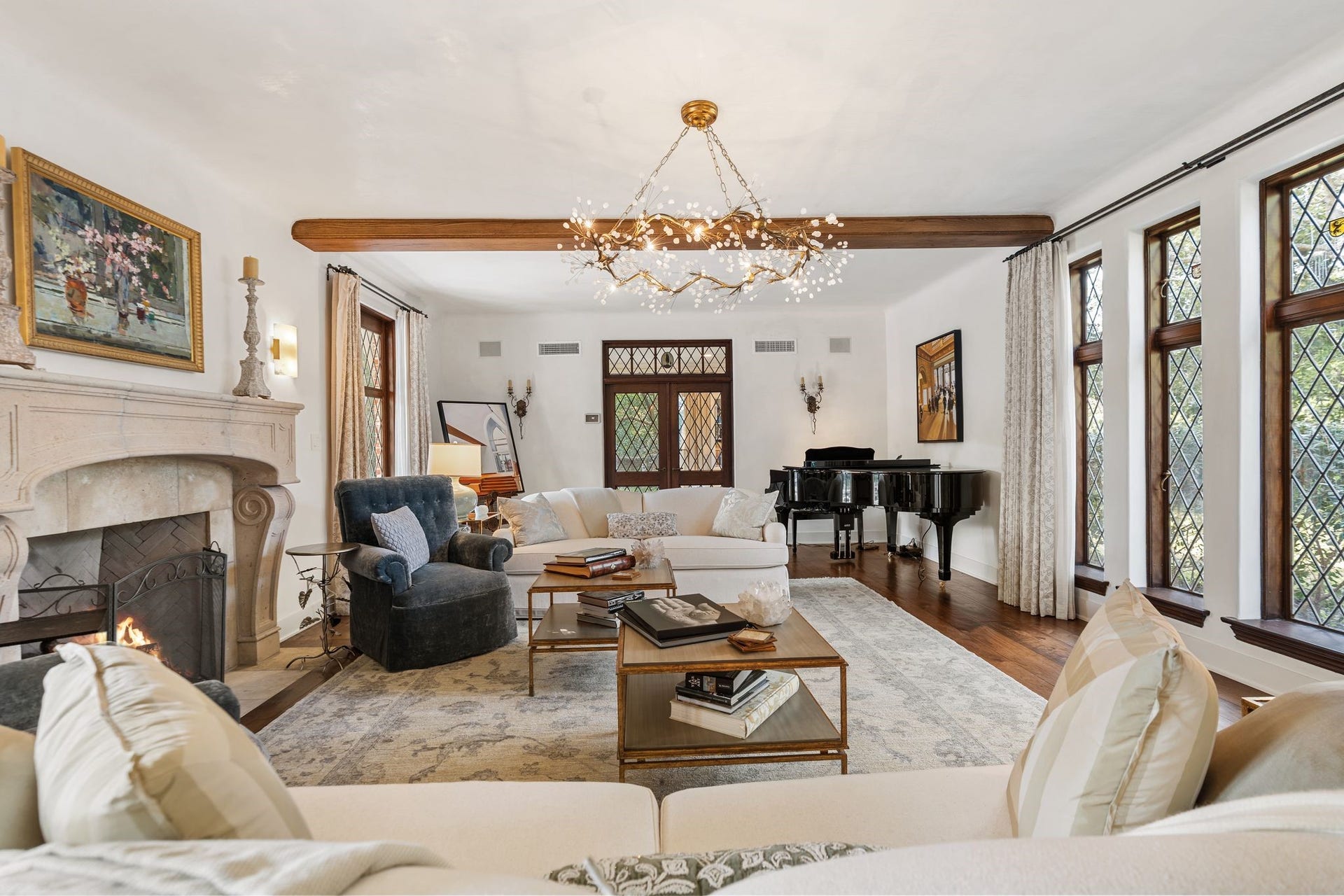 [Living Room]
This view reveals the living room's stone masonry fireplace. Leaded glass doors at rear open into a sunroom. Note painted-glass heraldic shields in upper windows.