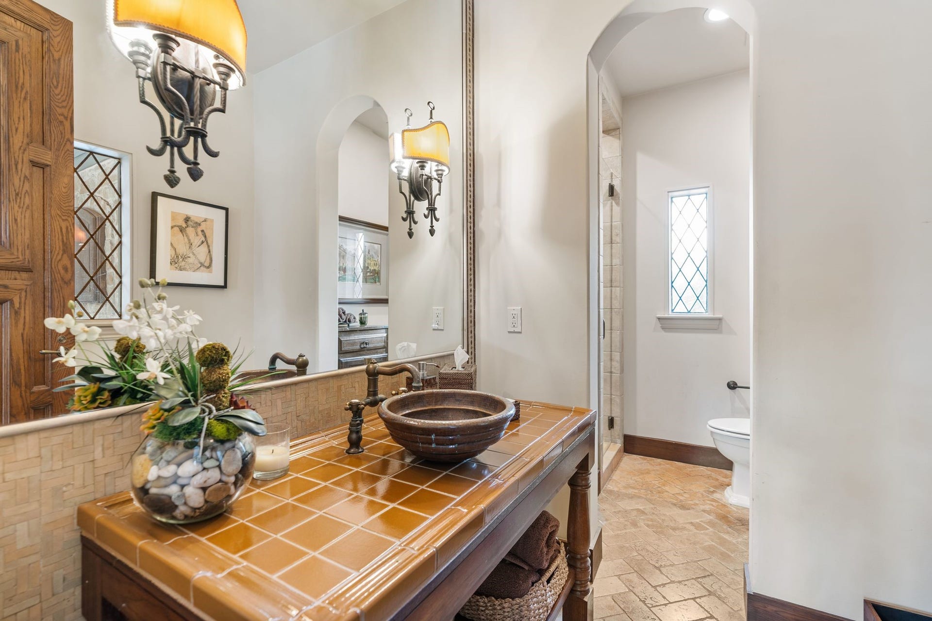 [Pool Bath]
Positioned beside the family room's rear exterior doors, this full bath serves the pool and pavilion. Note herringbone-patterned brick floor, seamless-glass shower door (left), and copper vessel sink.