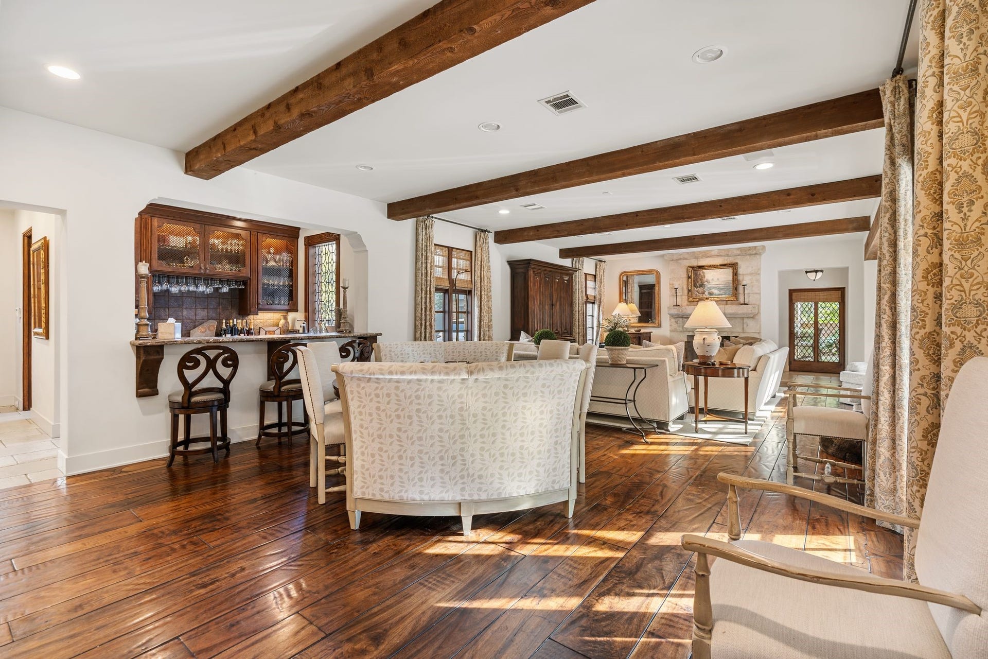 [Family Room]
A wide-plank hardwood floor extends across the family room where full-length reproduction leaded glass windows provide patio and pool views on one side and driveway/motor court views on the other. An interior window in the full bar has a serving ledge. Leaded glass double doors at rear open to the outdoor pavilion and a breezeway to the driveway and motor court.